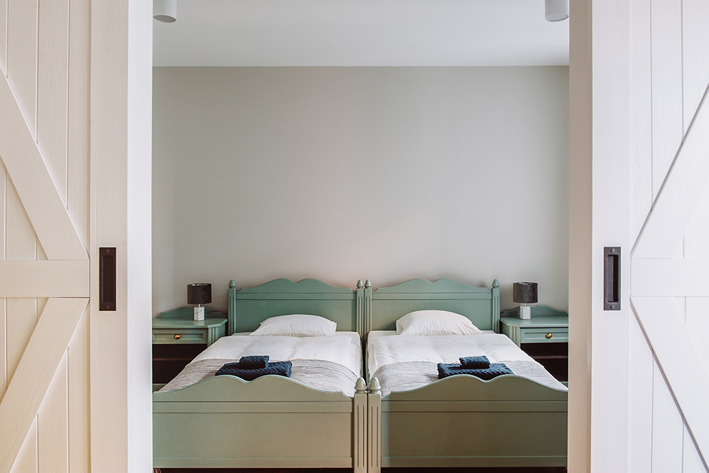 ein großes salbeifarbenes Bett hinter einer weißen Doppeltür