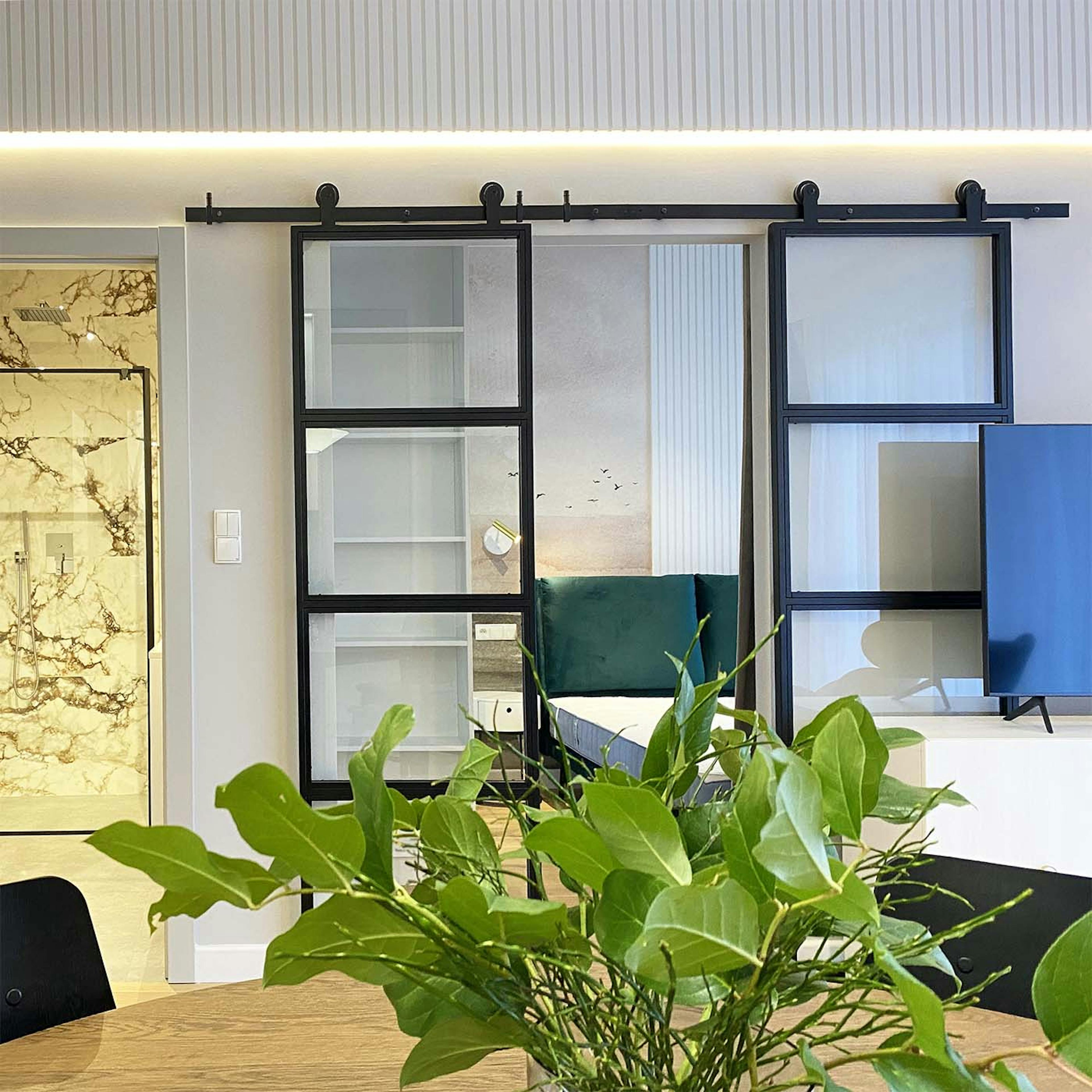 Doppelschiebetüren aus Metall mit Glas, die das Wohnzimmer vom Schlafzimmer in einer modernen Wohnung trennen