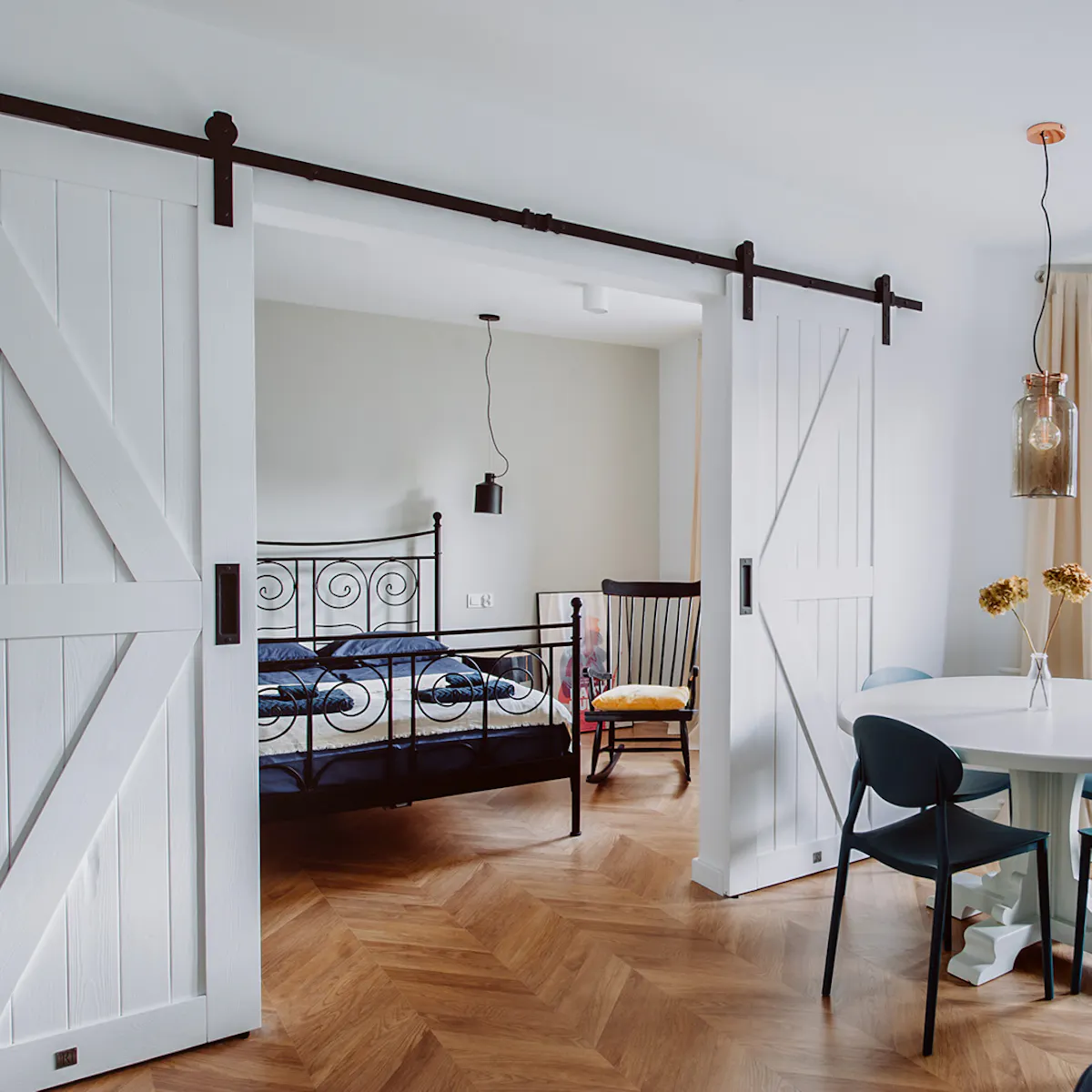 styl modern retro, apartamenty do wynajęcia Wrocław, drzwi przesuwne dwuskrzydłowe, drzwi przesuwne podwójne, drzwi przesuwne białe, drzwi przesuwne barn door, otwarta przestrzeń, podwójne drzwi do sypialni, łóżko do sypialni w stylu retro, fotel bujany w sypialni