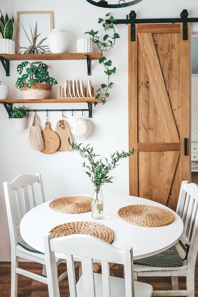 Holzregal für Küchenzubehör, schmale Holzschiebetür, Dekorationen im Boho-Stil, weißer runder Tisch in der Küche, weißer Tisch und weiße Stühle, Holzaccessoires in der Küche
