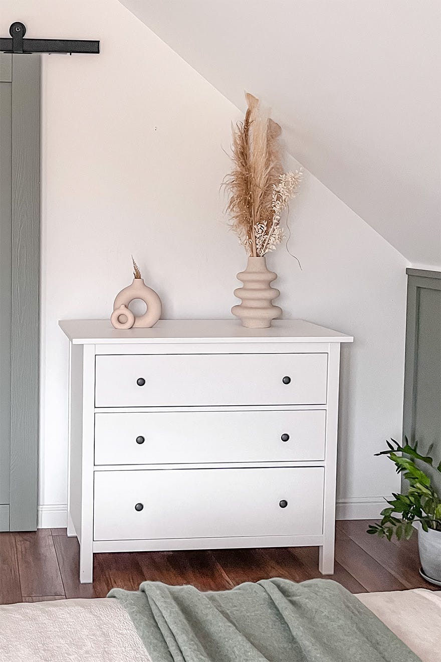 biała komoda w stylu skandynawskim stojąca pod skośnym sufitem