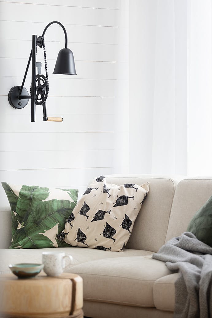 schwarze Industrielampe an weißer Wand, hellbraunes Sofa, dekorative Kissen