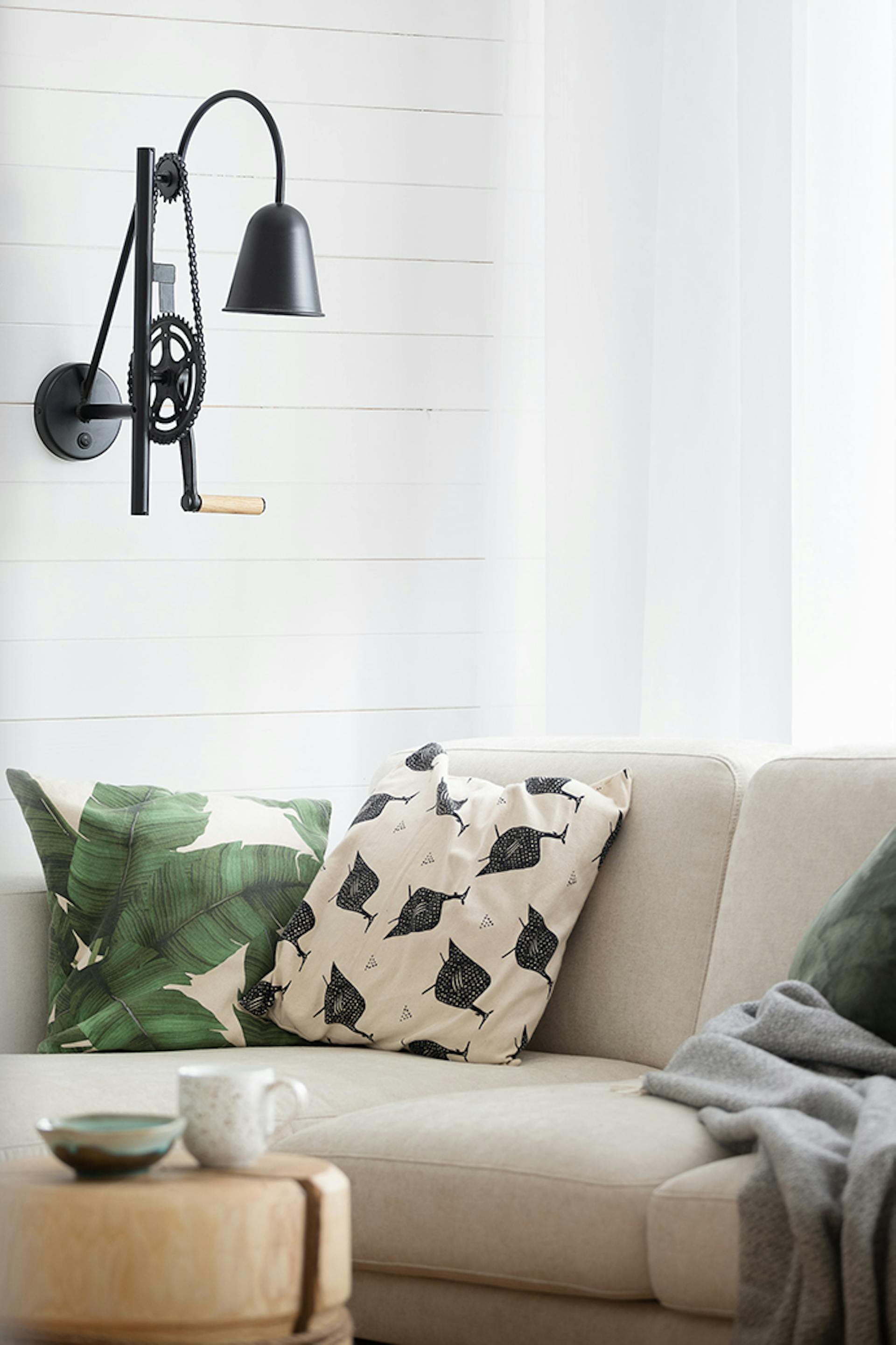 schwarze Industrielampe an weißer Wand, hellbraunes Sofa, dekorative Kissen