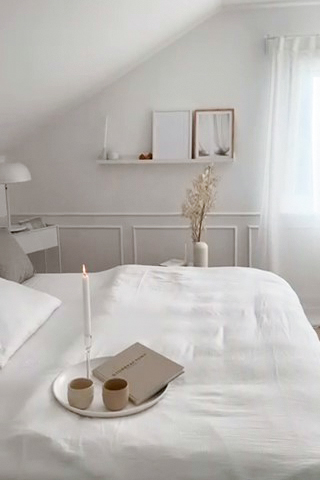 Weiße Bettwäsche auf einem großen Bett unter der Dachschräge im Schlafzimmer im Dachgeschoss