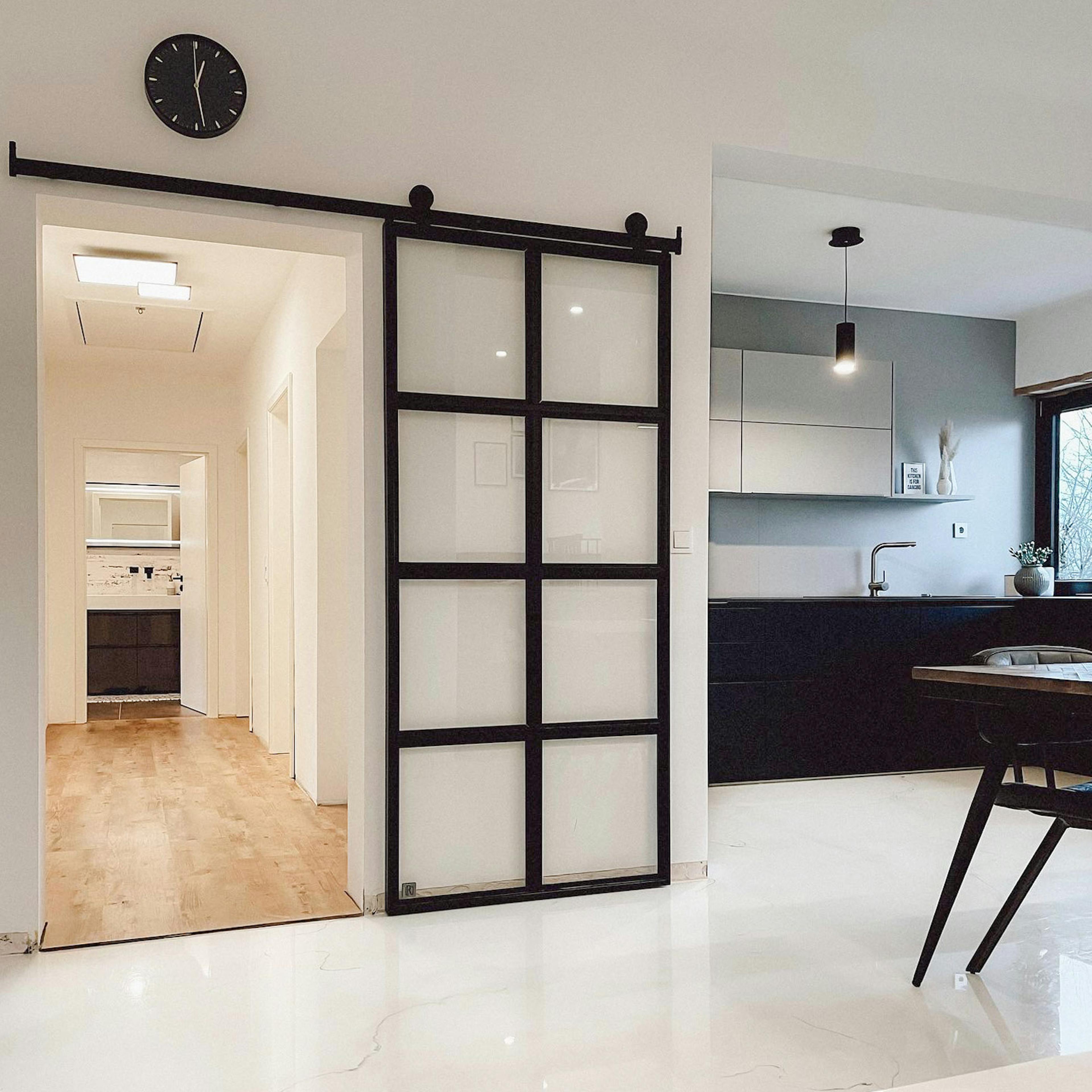 Glasschiebetüren, Metalltür mit transparentem Glas, schwarz-weiße offene Küche, schwarze Uhr an der weißen Wand