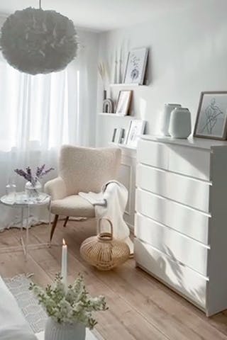 eine weiße Kommode und ein cremefarbener Sessel am Fenster im Schlafzimmer