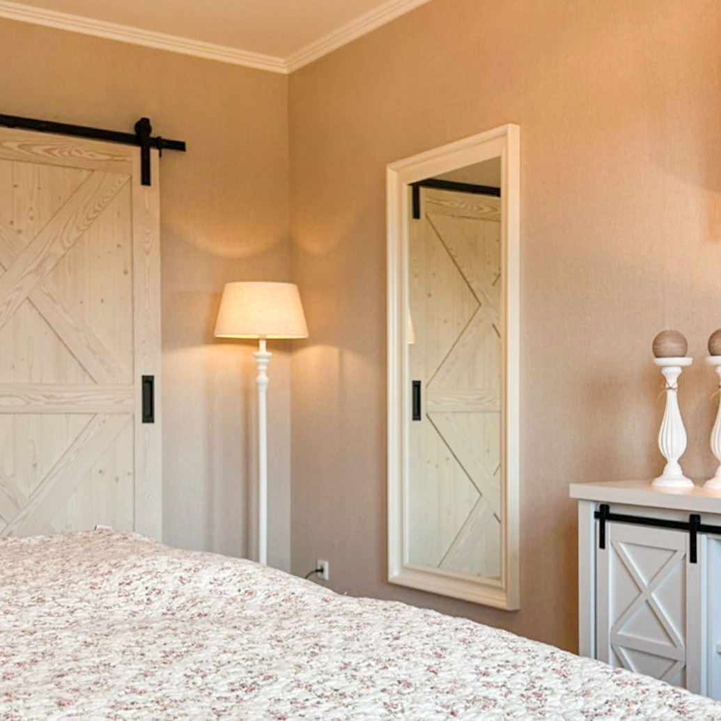 Ein großer Spiegel mit weißem Rahmen und eine weiße Schiebetür in einem Schlafzimmer im modernen Landhausstil