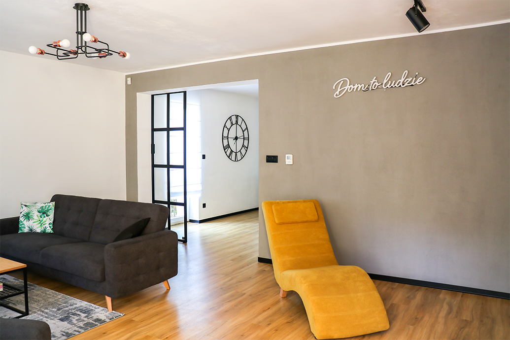 offenes Wohnzimmer, graues Sofa im Wohnzimmer, Industrielampe im Wohnzimmer, gelber Sessel für das Wohnzimmer, graue Wand im Wohnzimmer, Wohnzimmer offen zum Esszimmer, Metalltür mit Glas, Schiebetür mit Glas, Tür im Loft-Stil, Leuchtreklame an der Wand, Neondekorationen