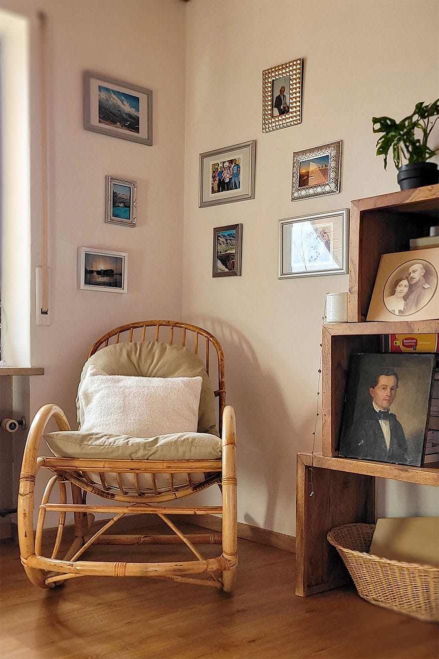 ein Schaukelstuhl aus Korbgeflecht an einer mit einer Fotogalerie geschmückten Wand
