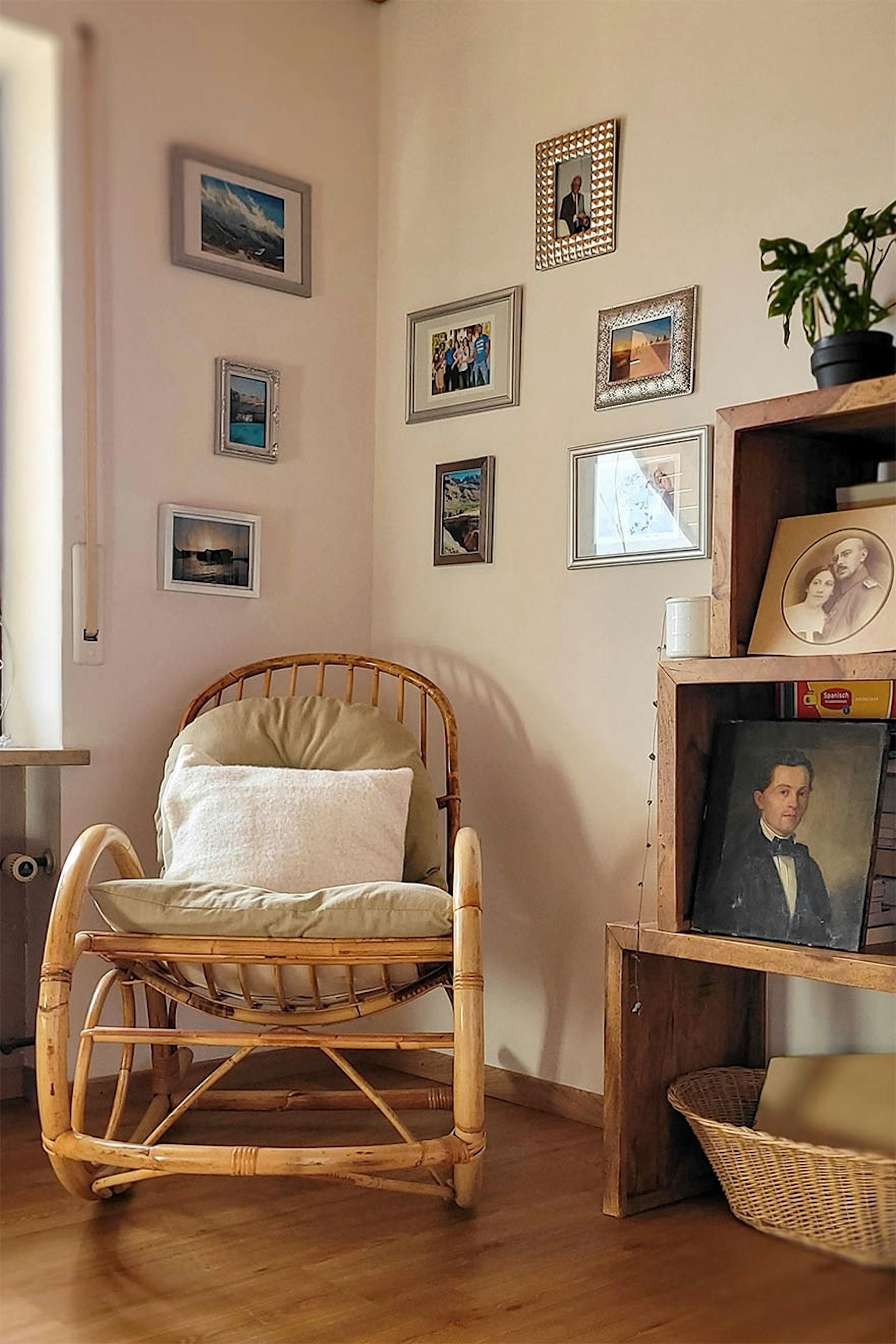 ein Schaukelstuhl aus Korbgeflecht an einer mit einer Fotogalerie geschmückten Wand
