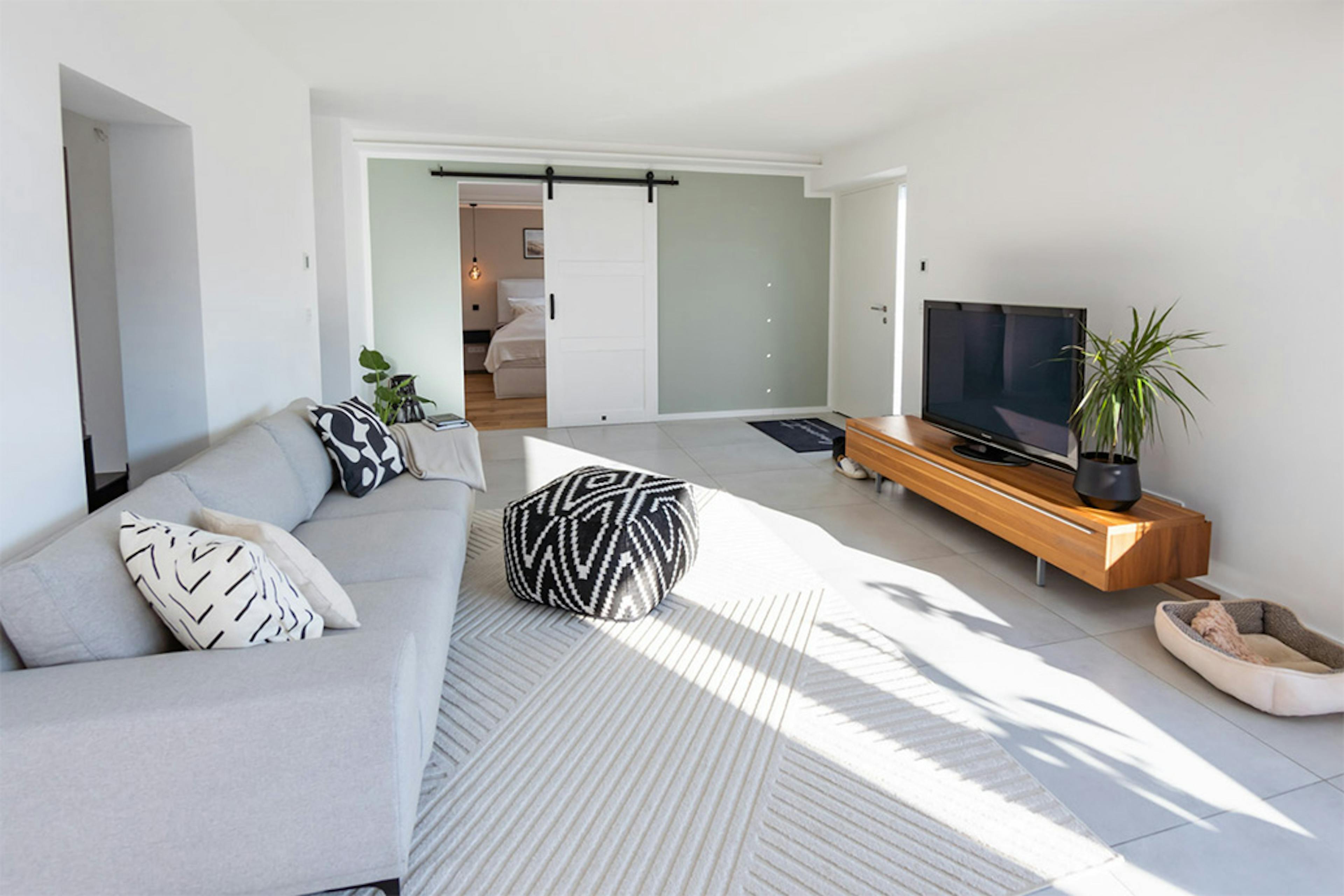 graues Sofa, dekorativer Puff, geometrische Muster auf Kissen, langer und niedriger TV-Ständer, Sitzecke in einem modernen Wohnzimmer