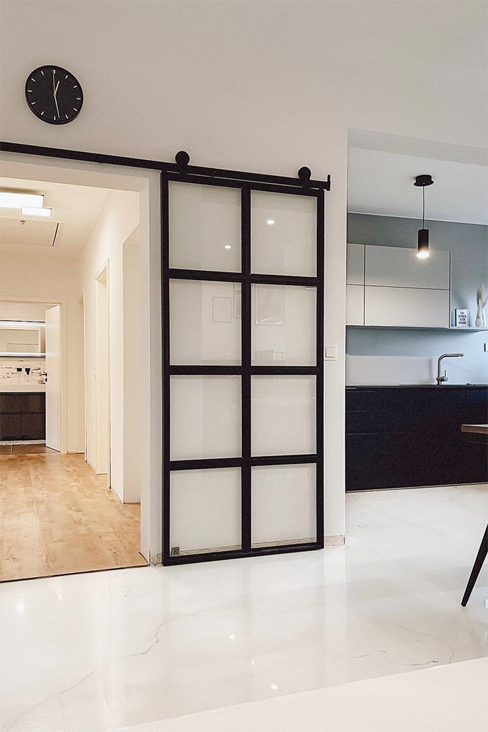 Glasschiebetüren, Metalltür mit transparentem Glas, schwarz-weiße offene Küche, schwarze Uhr an der weißen Wand