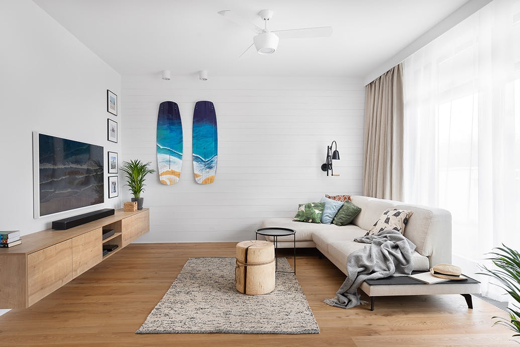 großes und helles Wohnzimmer, weiße Wände im Wohnzimmer, blaues dekoratives Surfbrett an der Wand, hölzerner Couchtisch, großes Sofa