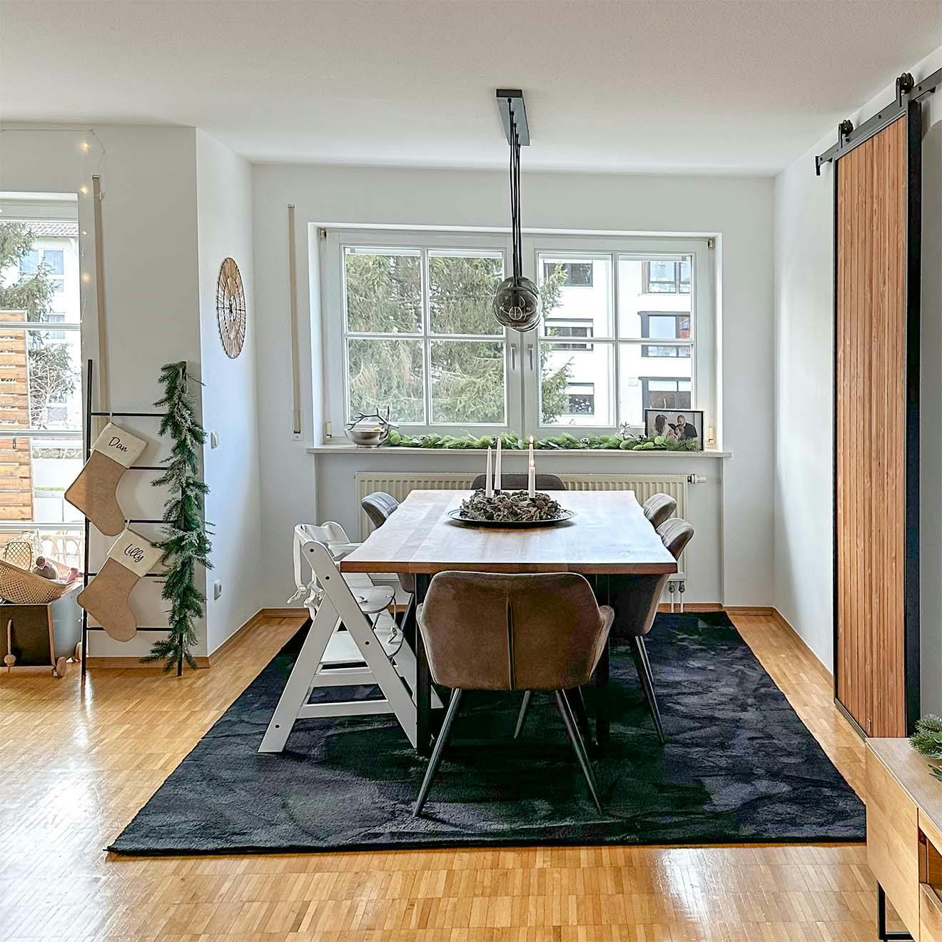 duży stół jadalniany na czarnym dywanie ustawiony obok dużego okna w salonie