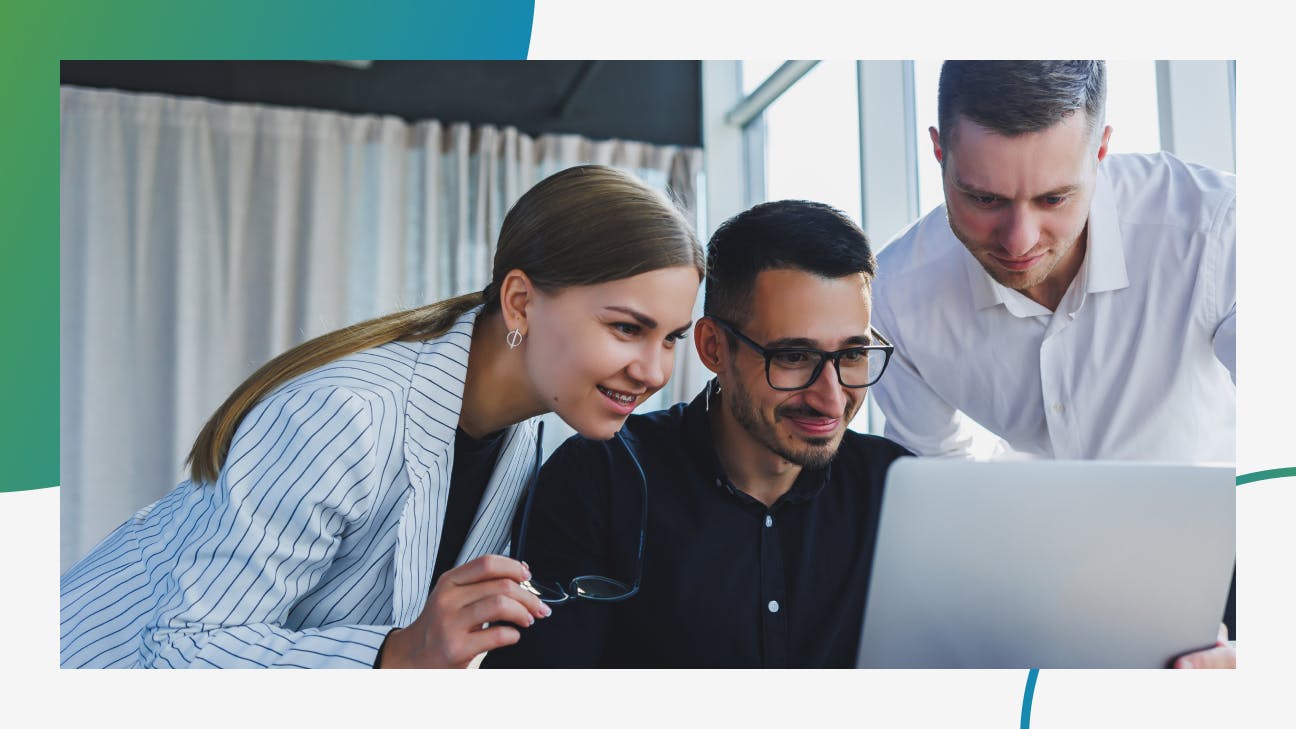 Three people sitting and standing around a laptop in an office environment