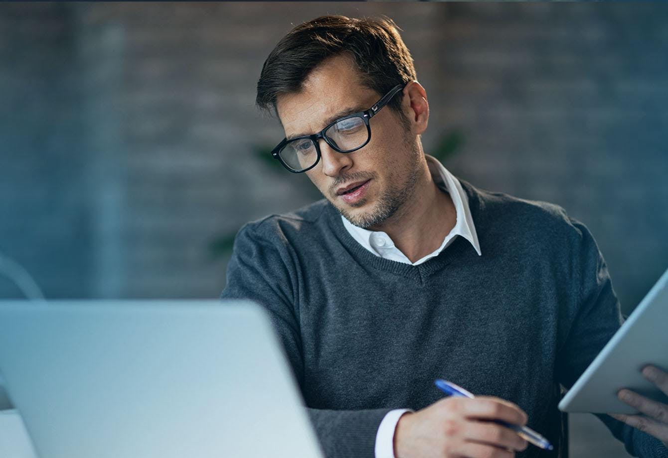 Adult male looking at a laptop holding a pen