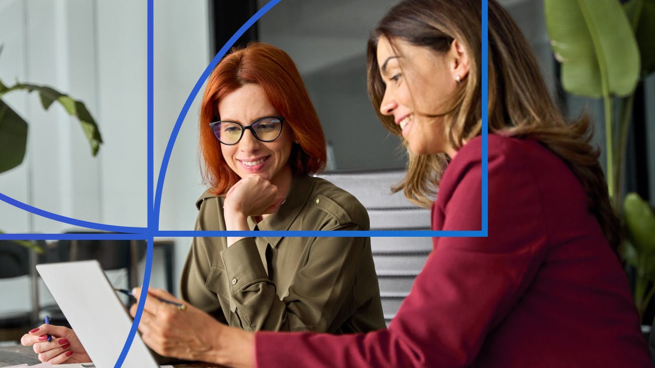 Two women sitting and smiling while looking at a laptop