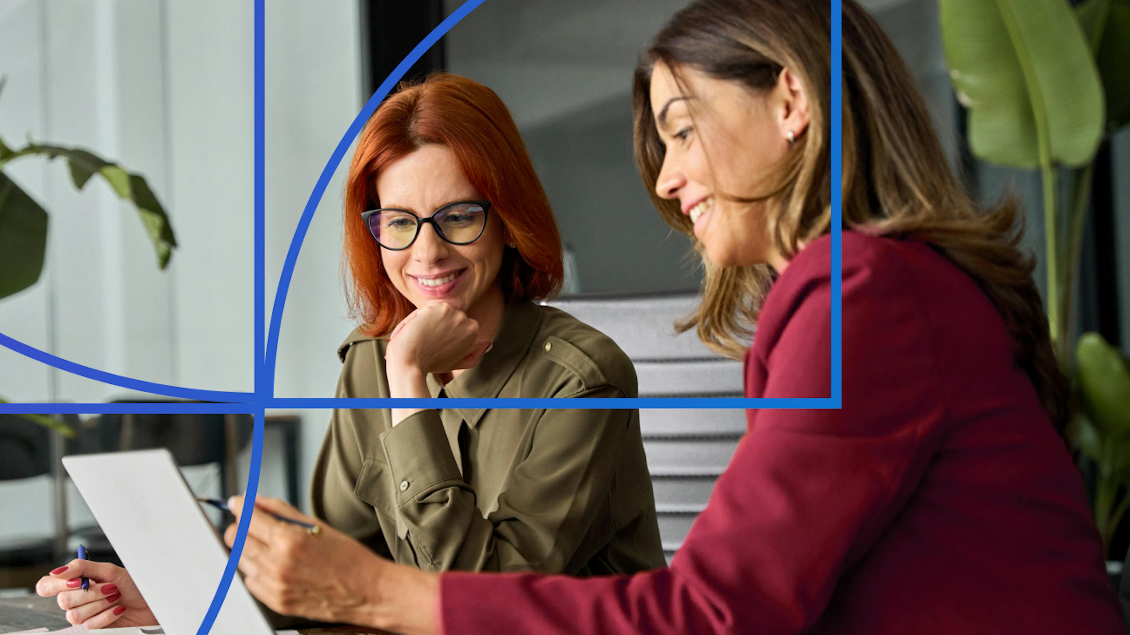 Two women sitting and smiling while looking at a laptop