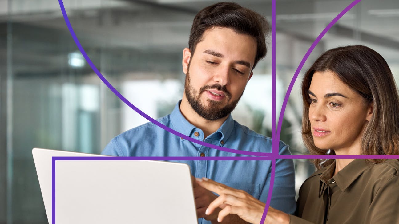 Man holding a laptop while woman stands to his right and points at laptop