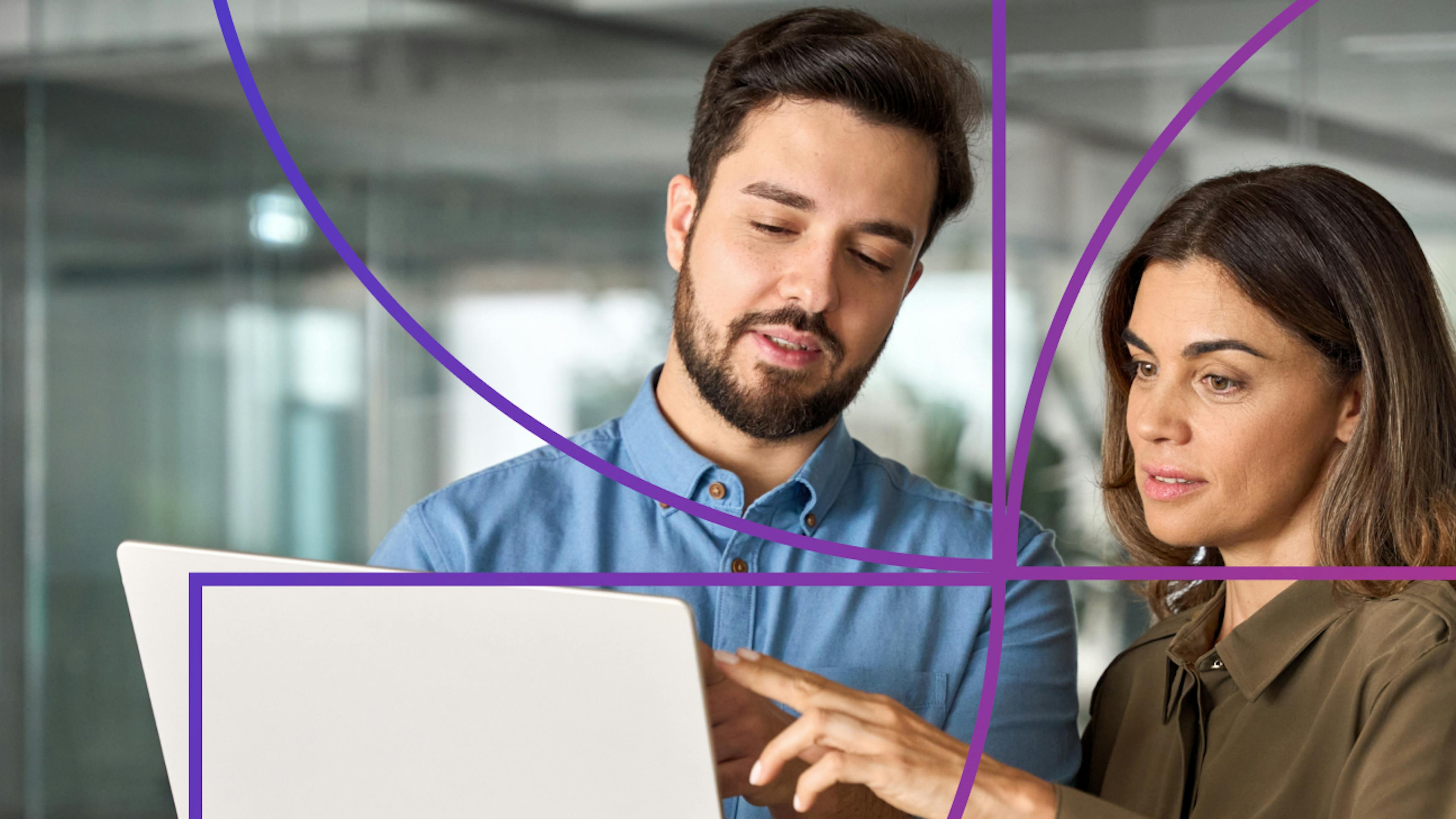 Man holding a laptop while woman stands to his right and points at laptop