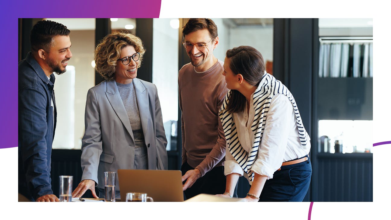 Four people standing around a laptop in an office setting
