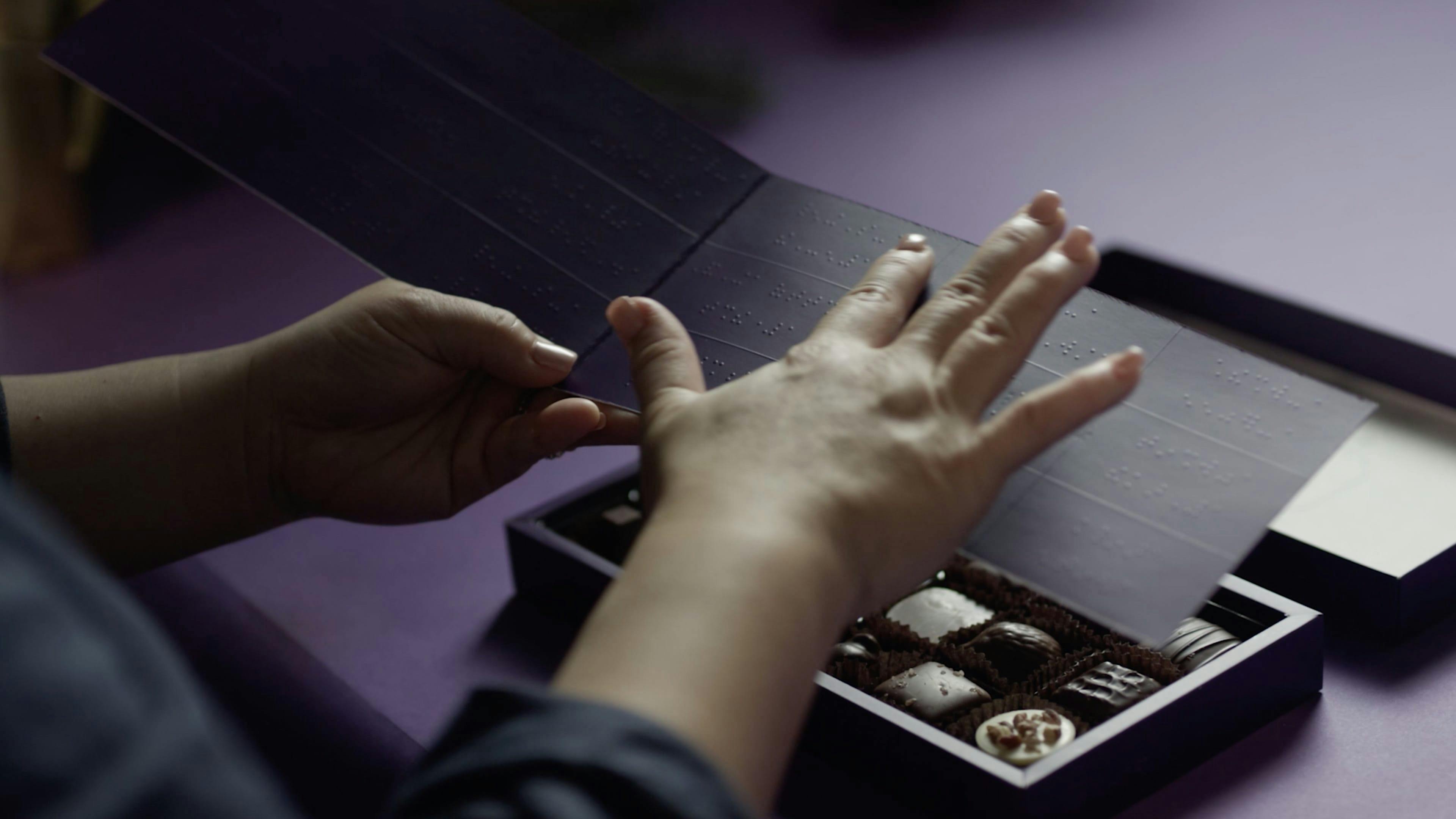 Fingers reading chocolate options in Purdy's braille box. 