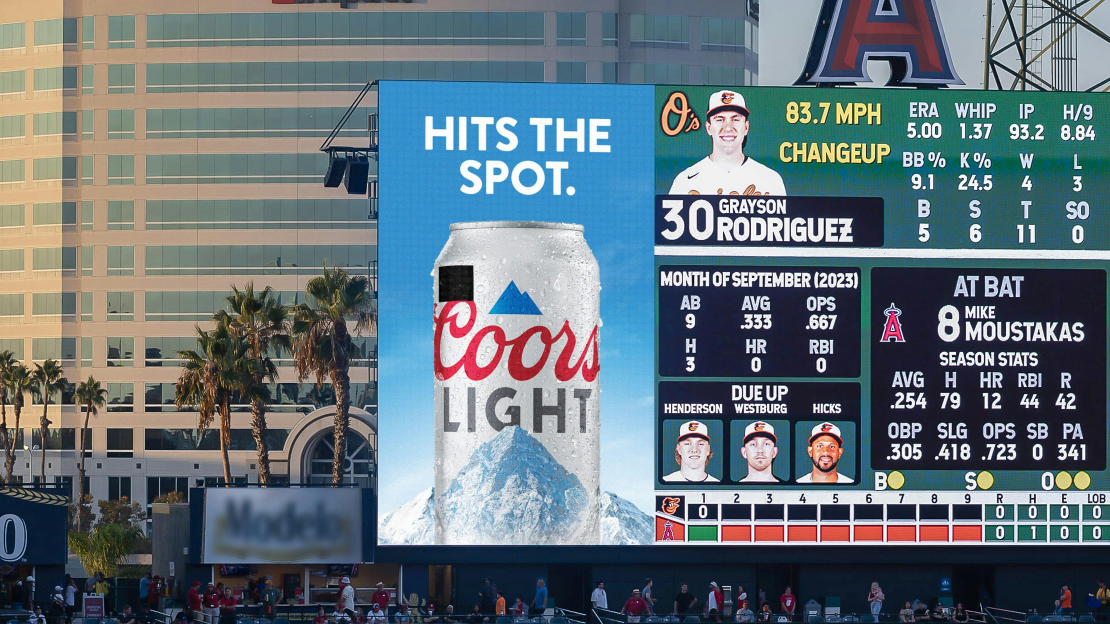 A Coors Light billboard at a baseball stadium during a live game, with an ad displaying a special-edition can that has a black square on the label.