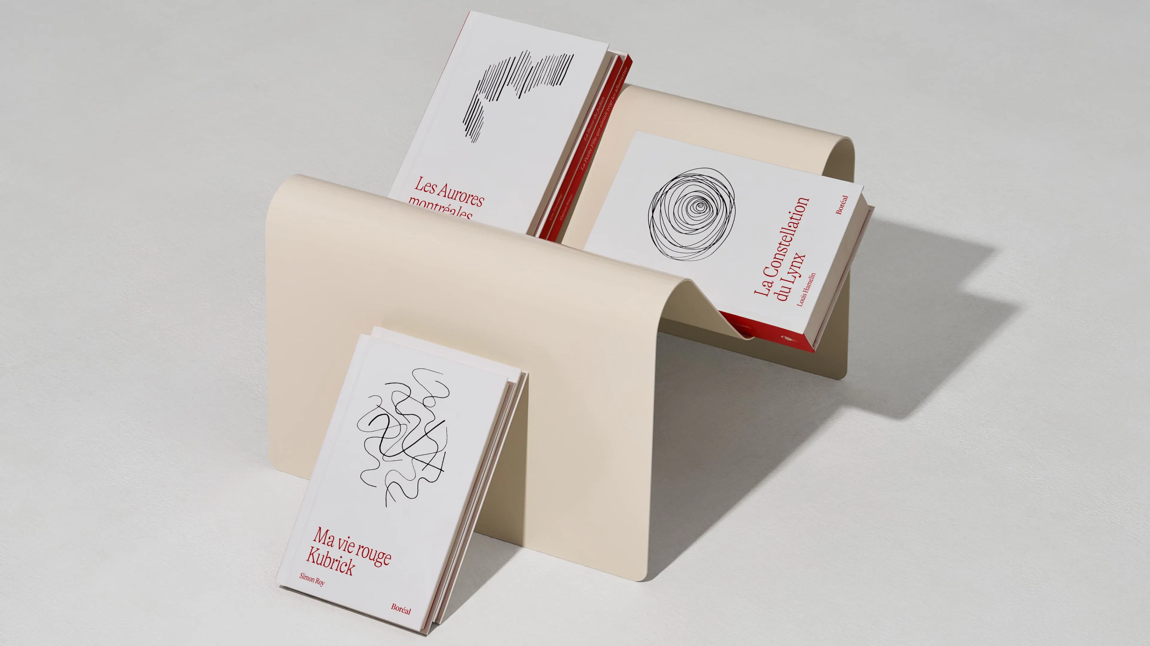 Three abstract design books with white covers and red text sit artistically on a cream, wave-shaped shelf.
