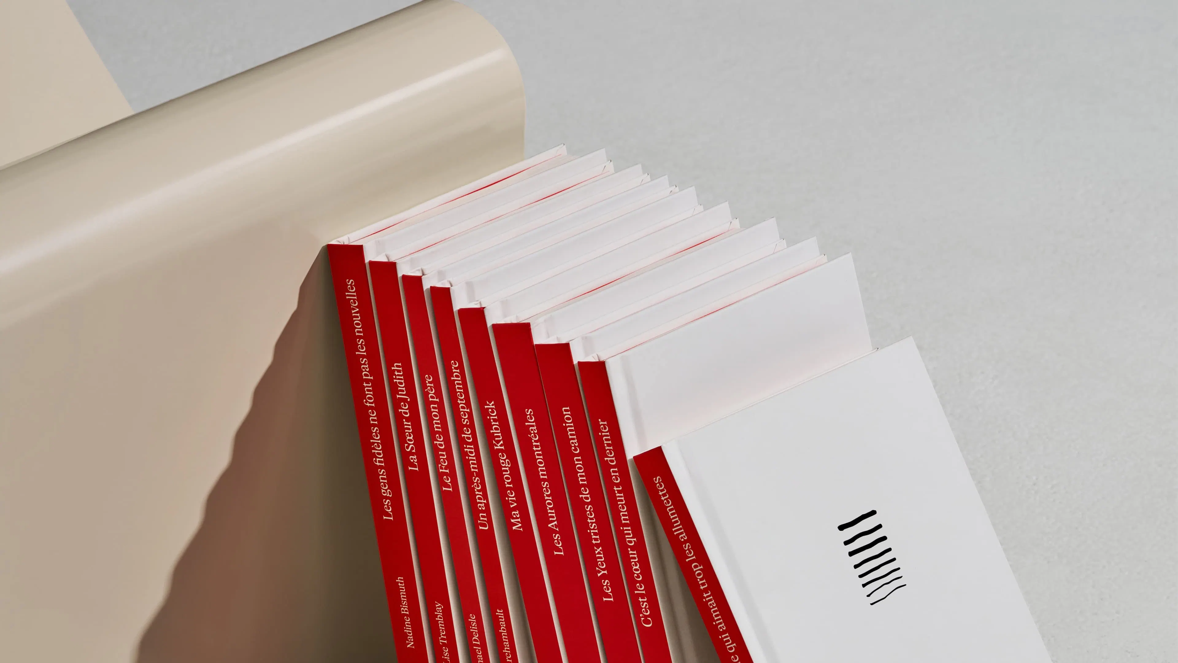 A stack of books with red spines and white covers leaning against a beige, curved surface.