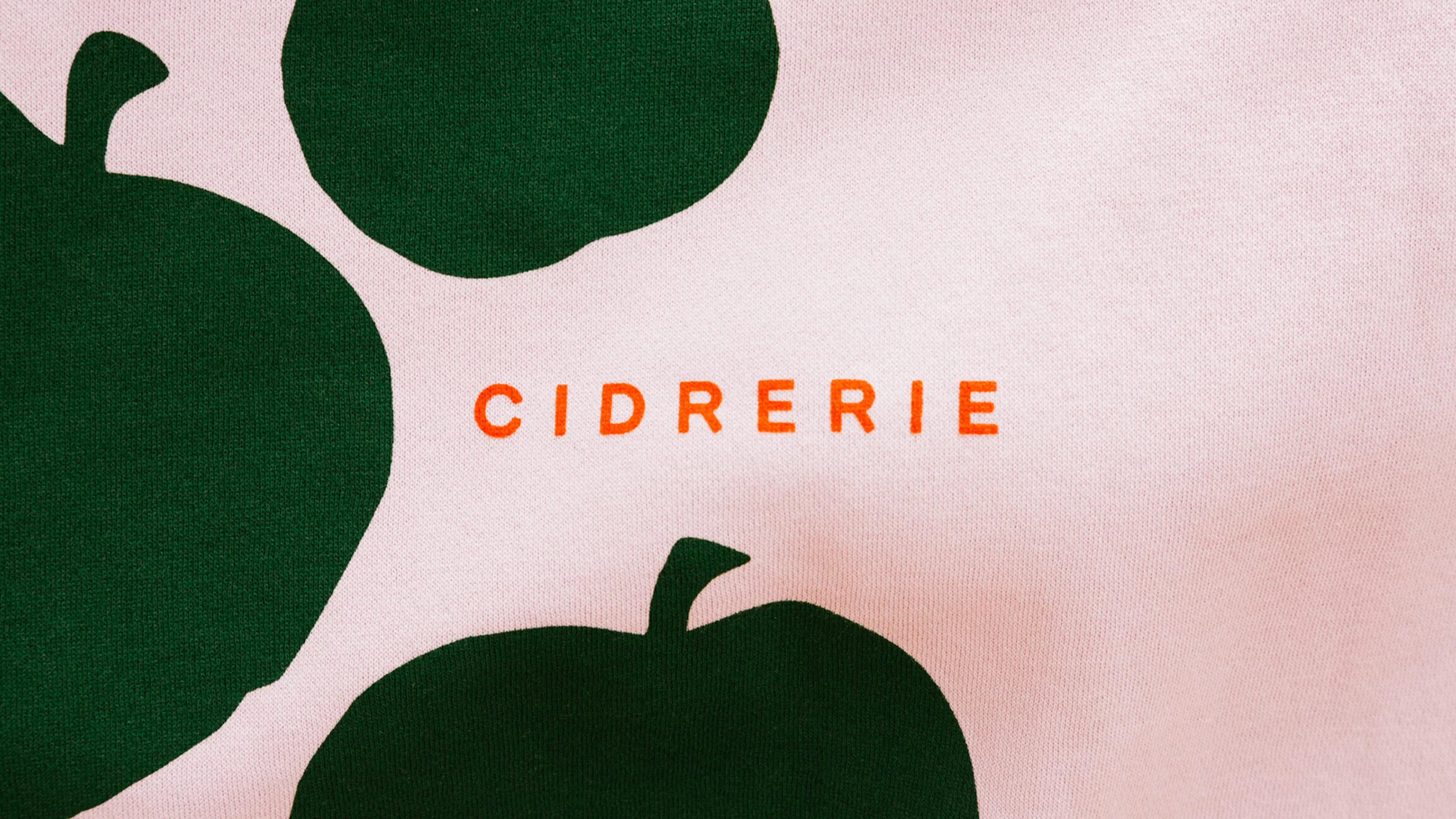 Bold green apple silhouettes on a soft pink background with "CIDRERIE" in orange text.