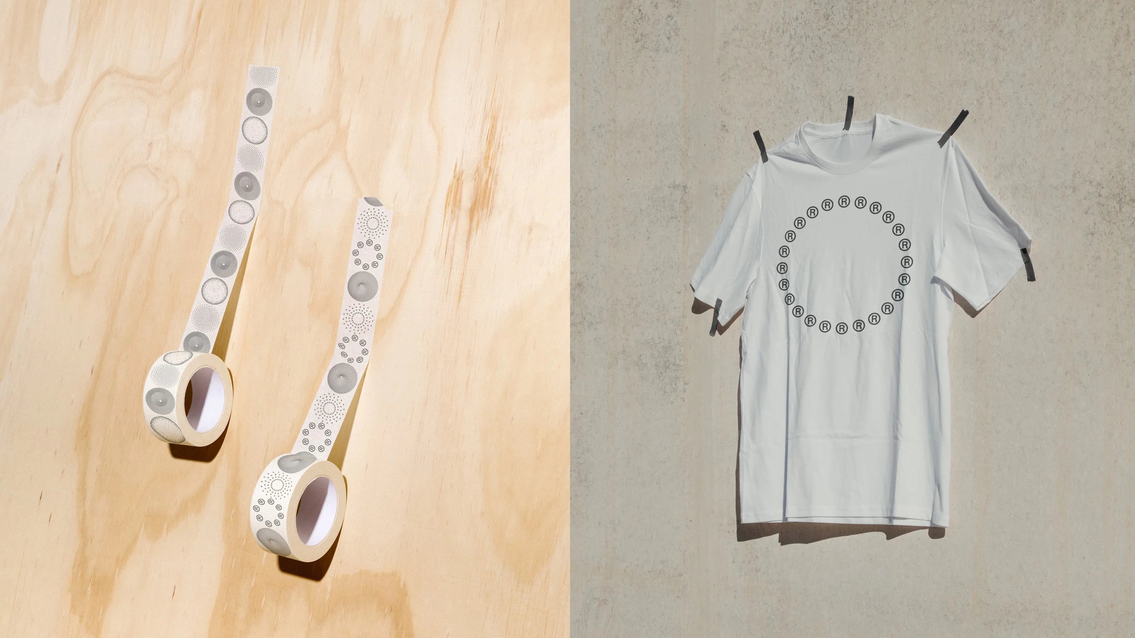 Two rolls of decorative tape with a registered trademark symbol pattern lay on a light wooden surface. Next to them, a white t-shirt with a similar design hangs on a textured wall.