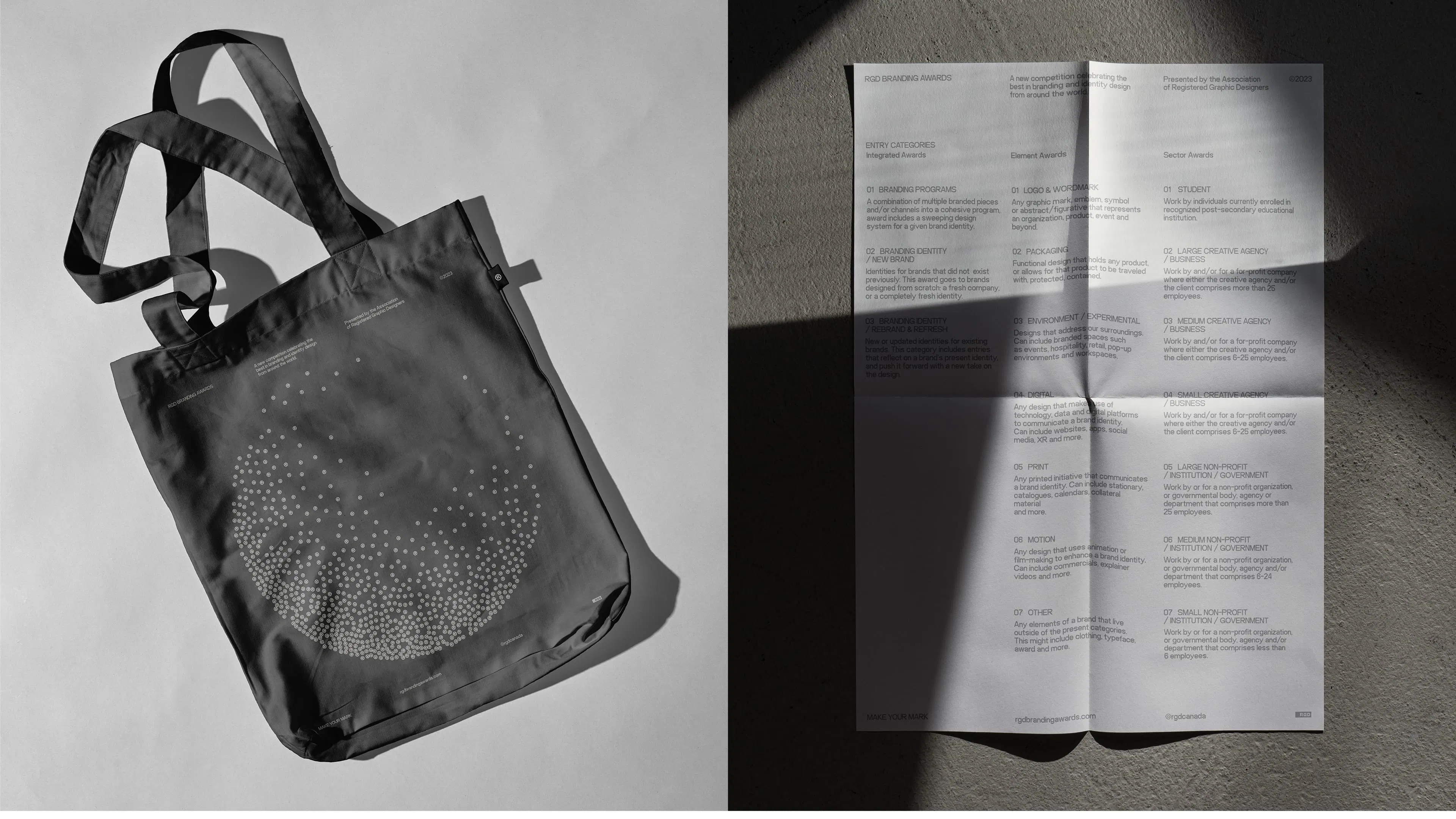 A gray tote bag with a circular pattern of white registered trademark symbols is on the left, its shadow cast on the surface. On the right, a folded, shadowed paper with text.