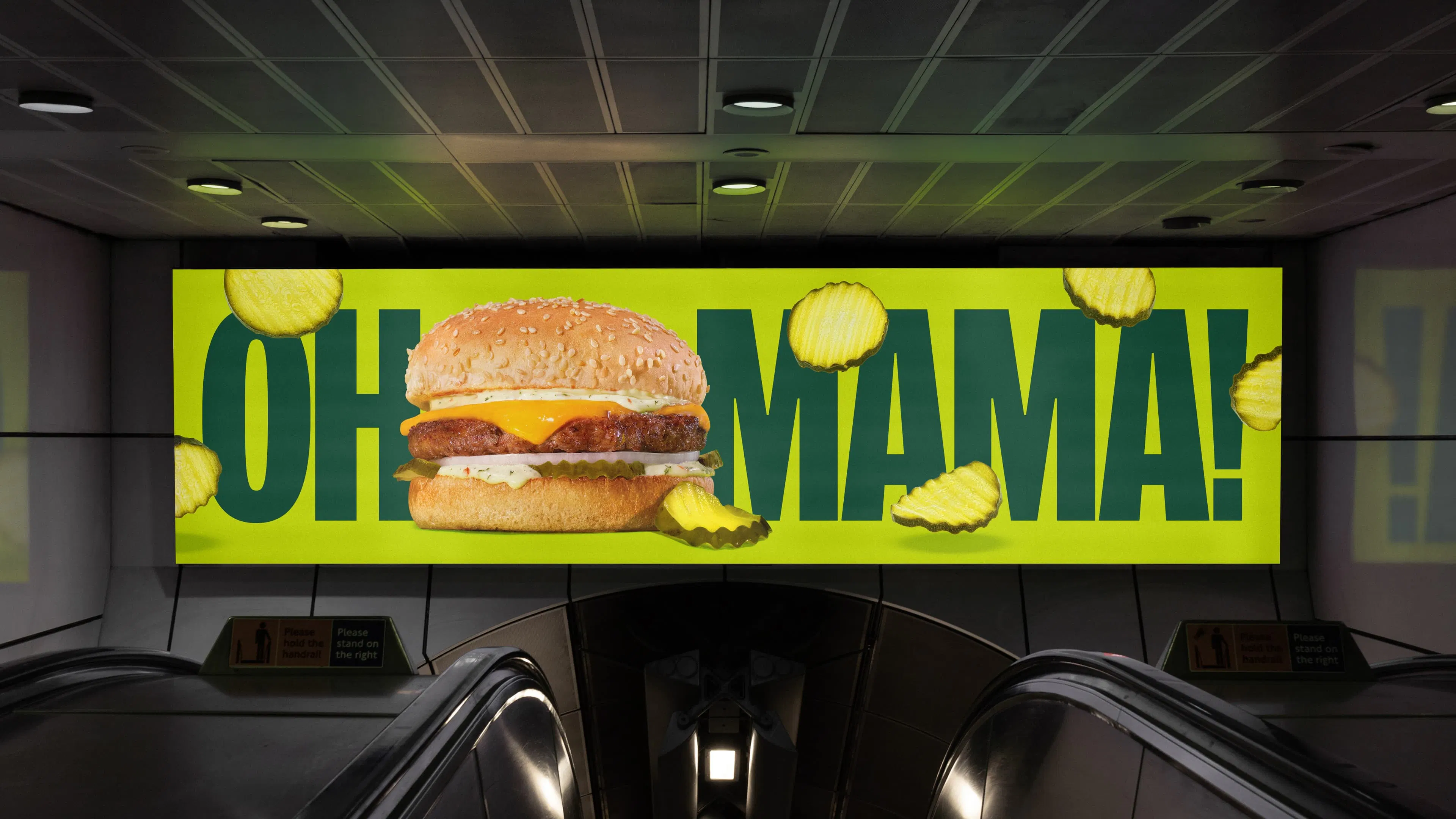 Digital billboard with an A&W Mama burger and bold text reading "OH MAMA!" on a bright lime green background with sliced pickles raining down.