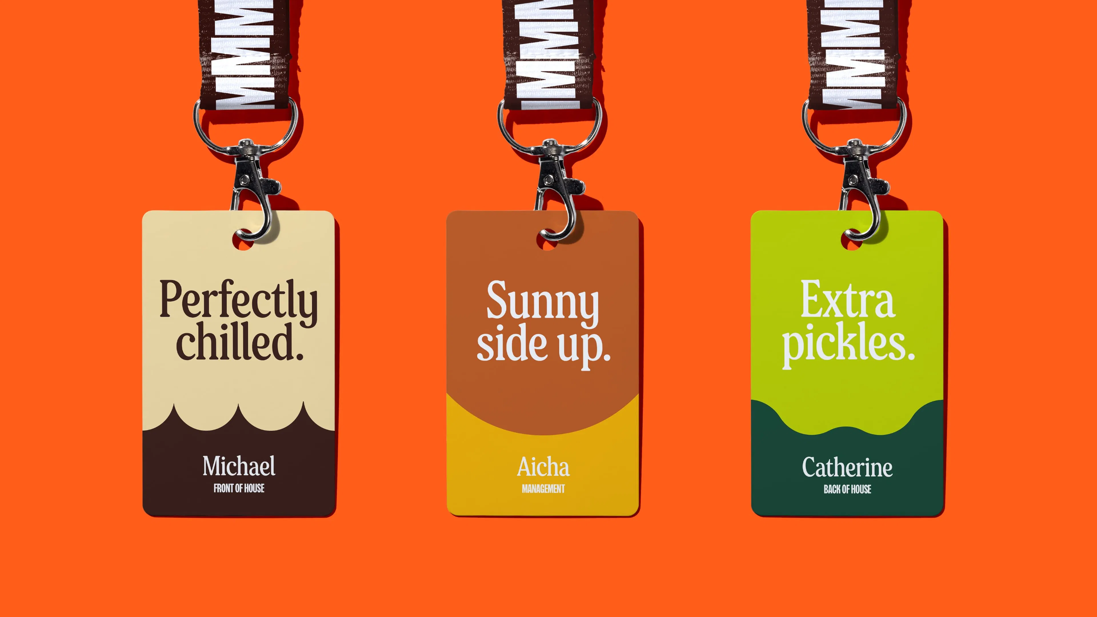 Three ID cards on lanyards with different colors and phrases on an orange background. Each has a graphic shape inspired by A&W food: root beer foam, an egg, and pickles.