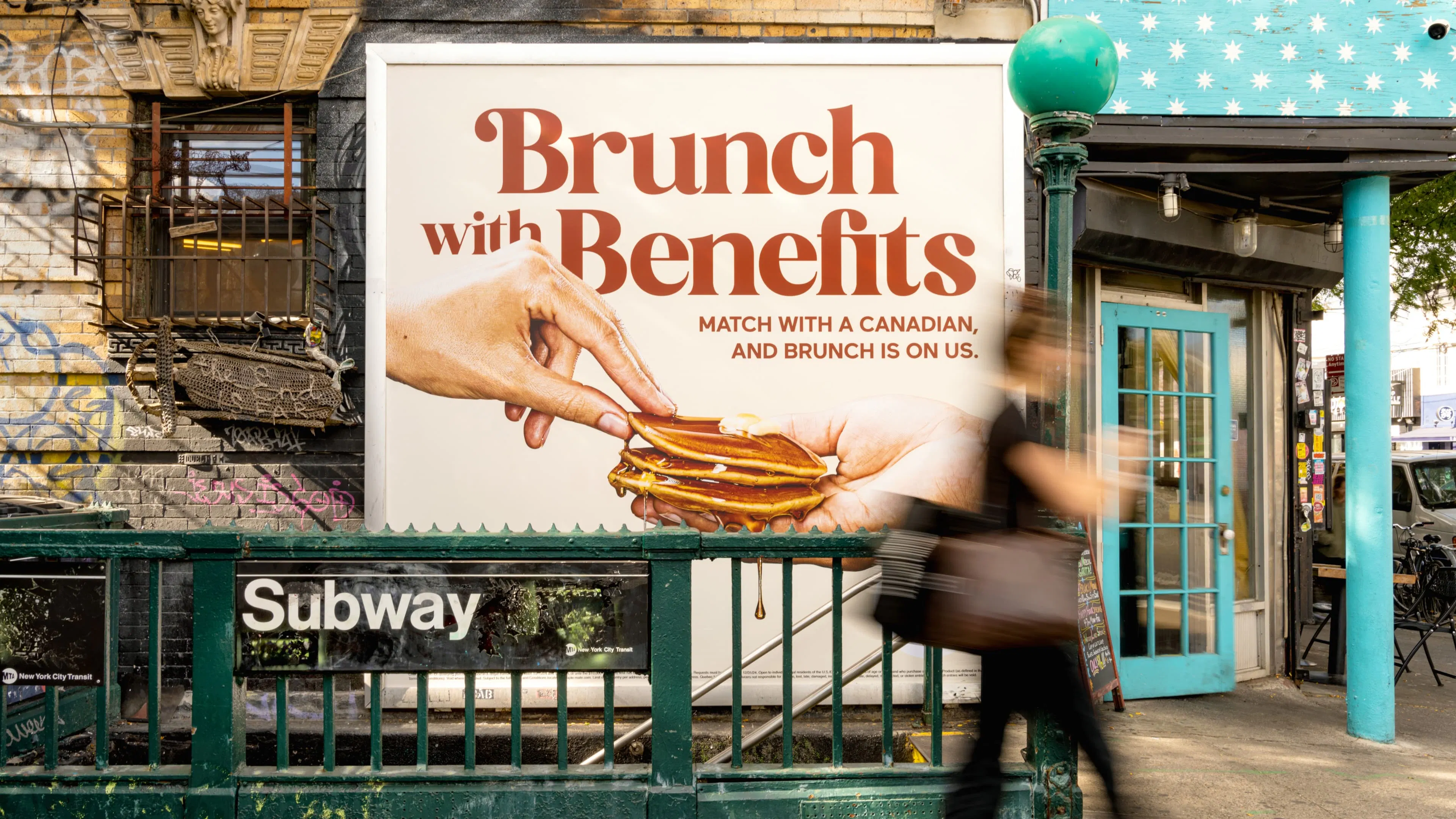 In a colourful urban scene, a passerby walks past New York City subway entrance sign and an out of home ad reading "Brunch with Benefits" featuring pancakes and maple syrup.
