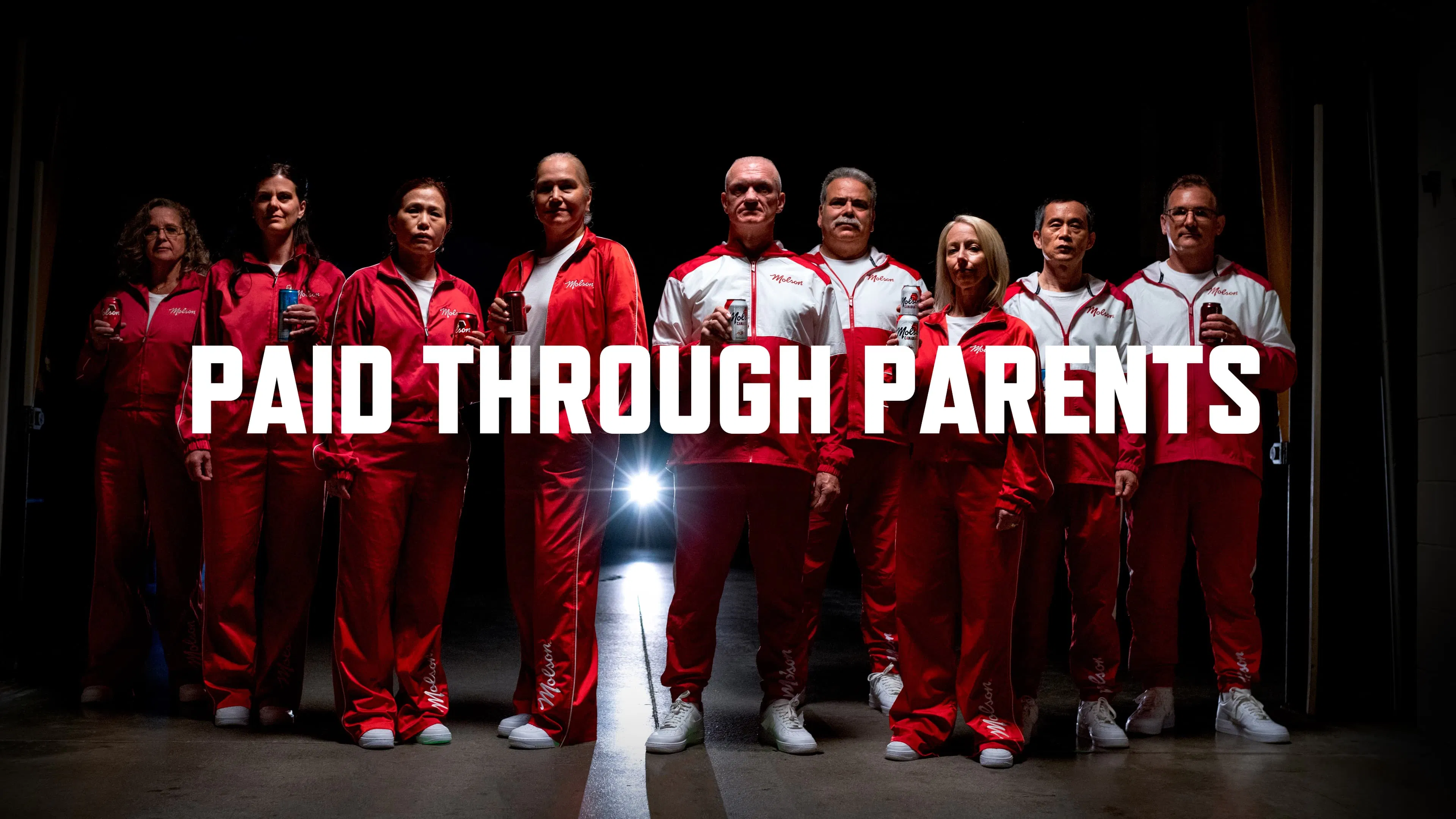 Nine parents stand on stage wearing red and white tracksuits in support of their children, who are Team Canada athletes.