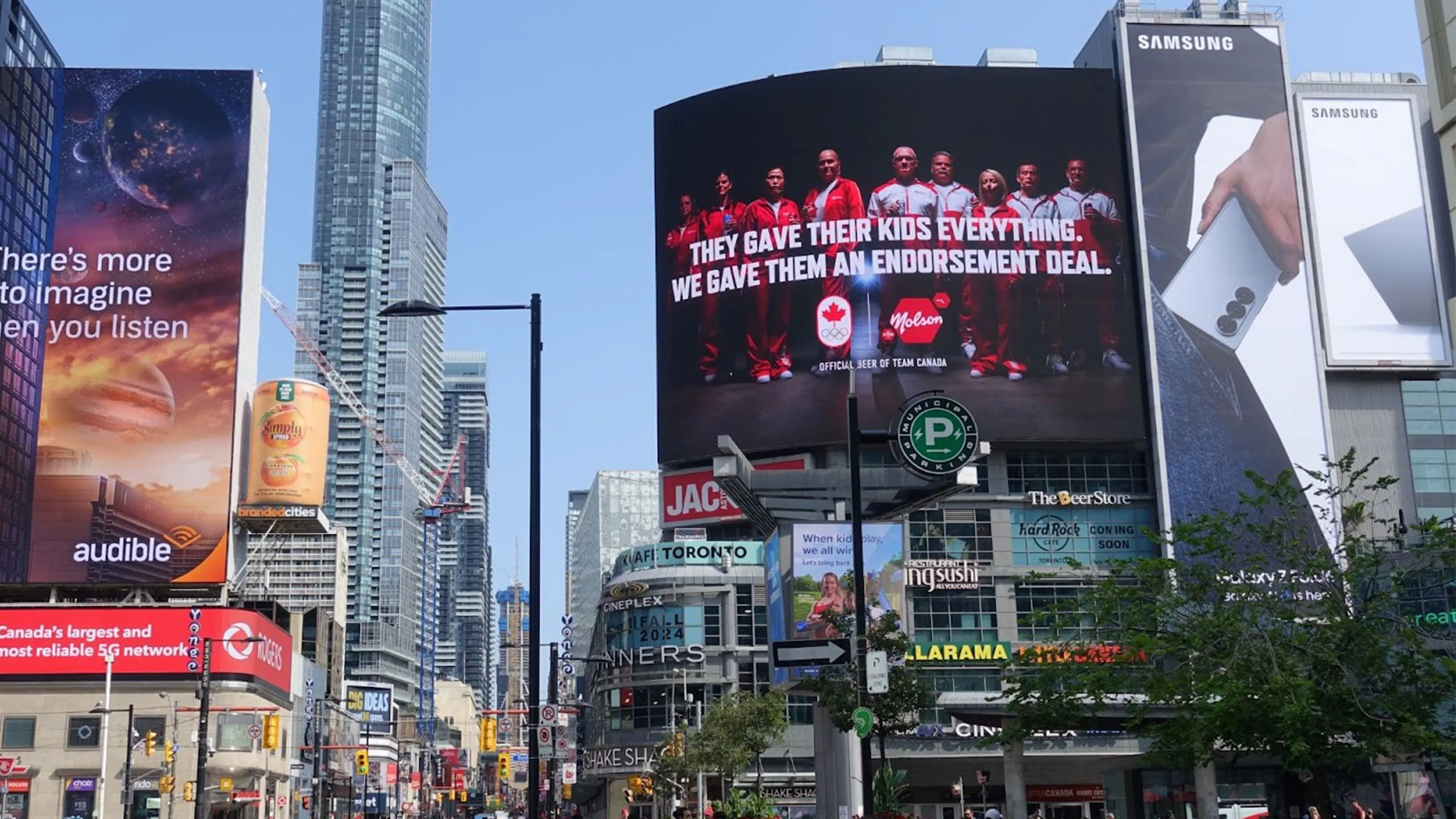 Out of home Molson Paid Through Parents advertisement on screen in a bustling city square.