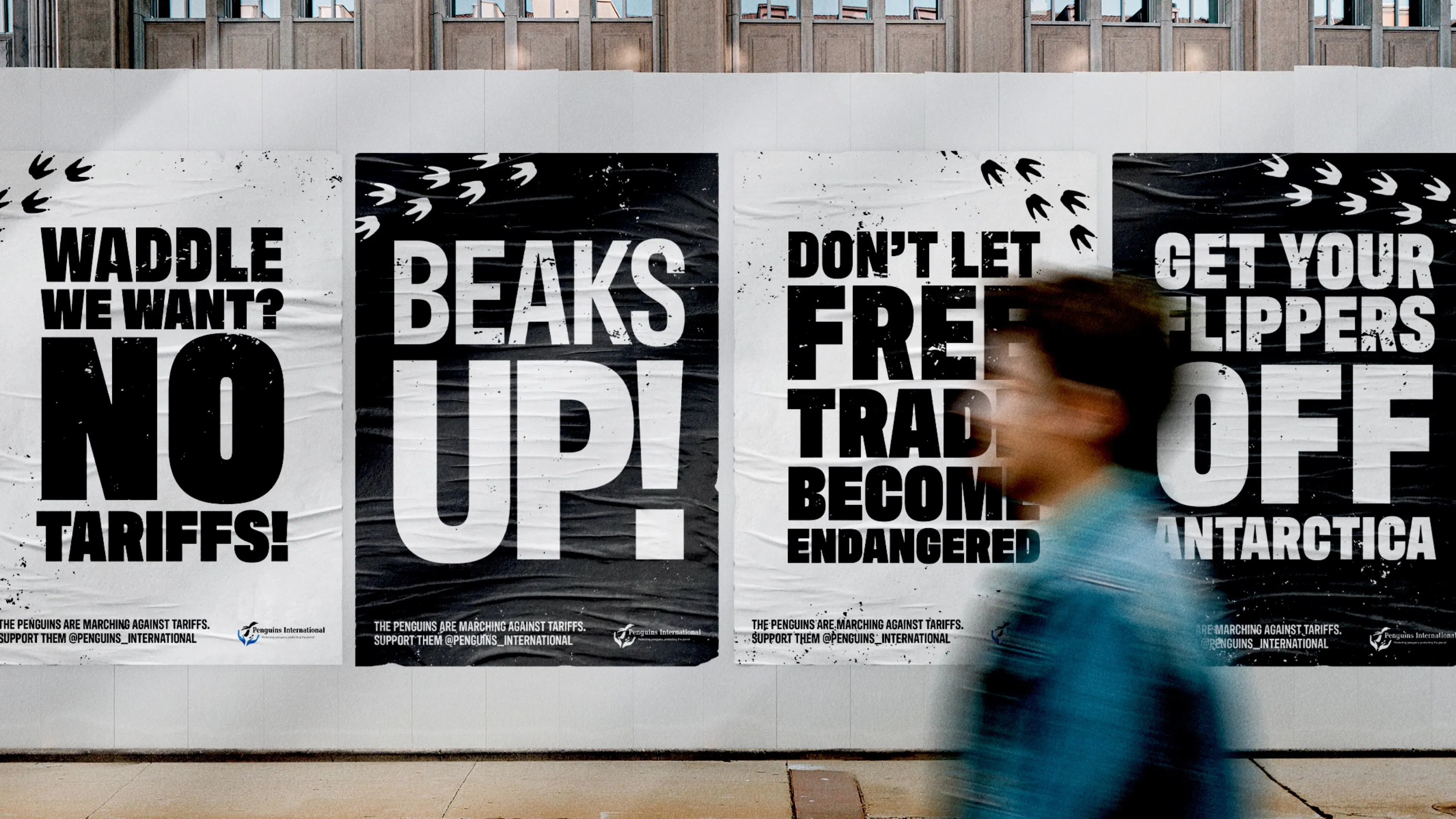 Out of home advertising boards on the street with a passerby in motion. The ads read “Waddle we want? No tariffs”, “Beaks up!”, “Don’t let free trade become endangered”, and “Get your flippers off Antarctica”. 