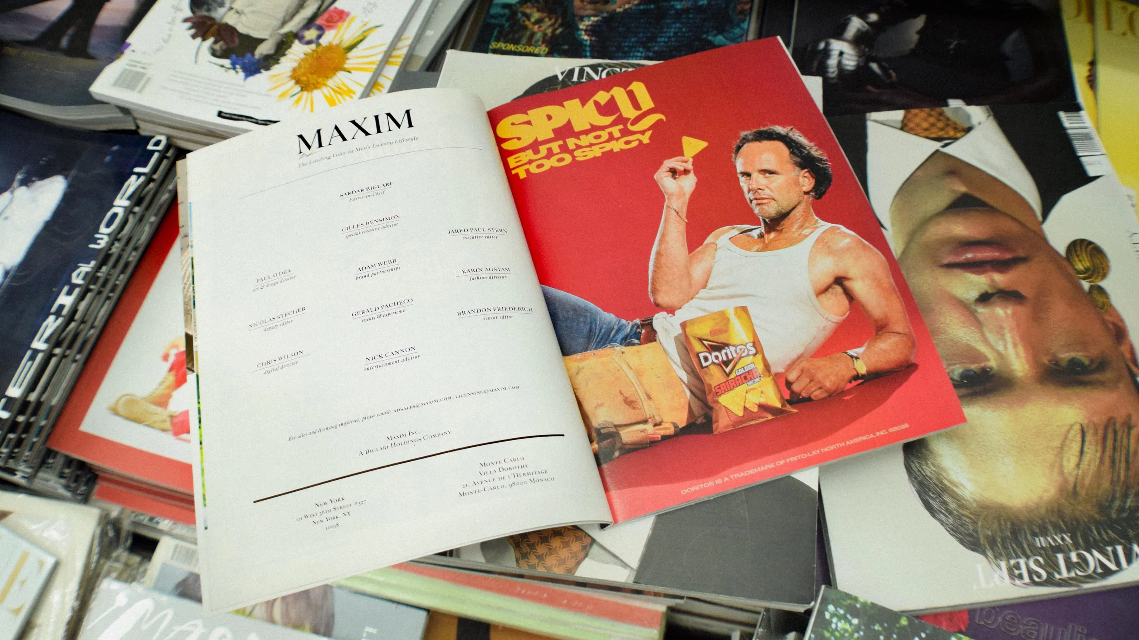 A variety of magazines sit a table. A page from Maxim magazine is left over with an ad for Doritos Golden Sriacha. Text reads Spidy But Not Too Spicy, next to actor Walter Goggings, playing a plumber, looks playful. He is wearing a white tank top, denim blue jeans, and a workbelt. He is holding a Dorito chip and a bag of Doritos is in front of them.