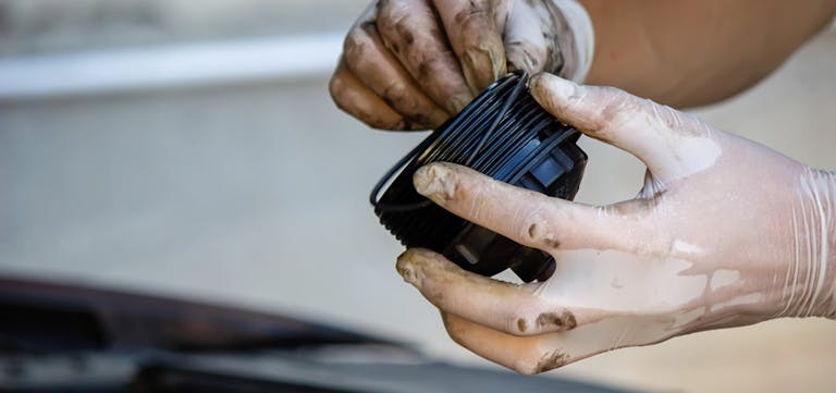 Nahaufnahme von Händen in Einweghandschuhe n, die einen verschmutzten Ölfilter halten. Symbolisch für einen Ölwechsell. Nahaufnahme von Händen in Einweghandschuhe n, die einen verschmutzten Ölfilter halten. Symbolisch für einen Ölwechsell.