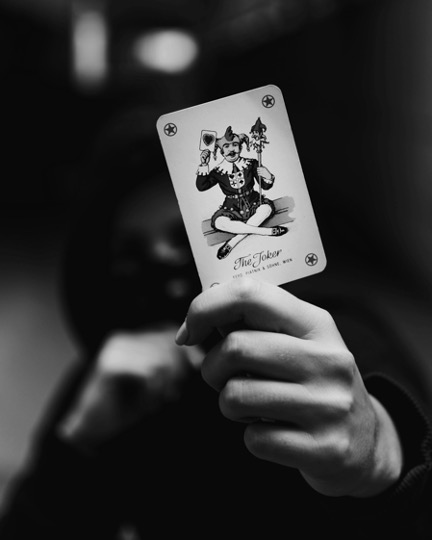 Eine Hand in Nahaufnahme, die eine Joker-Spielkarte hochhält, der Hintergrund ist schattig.