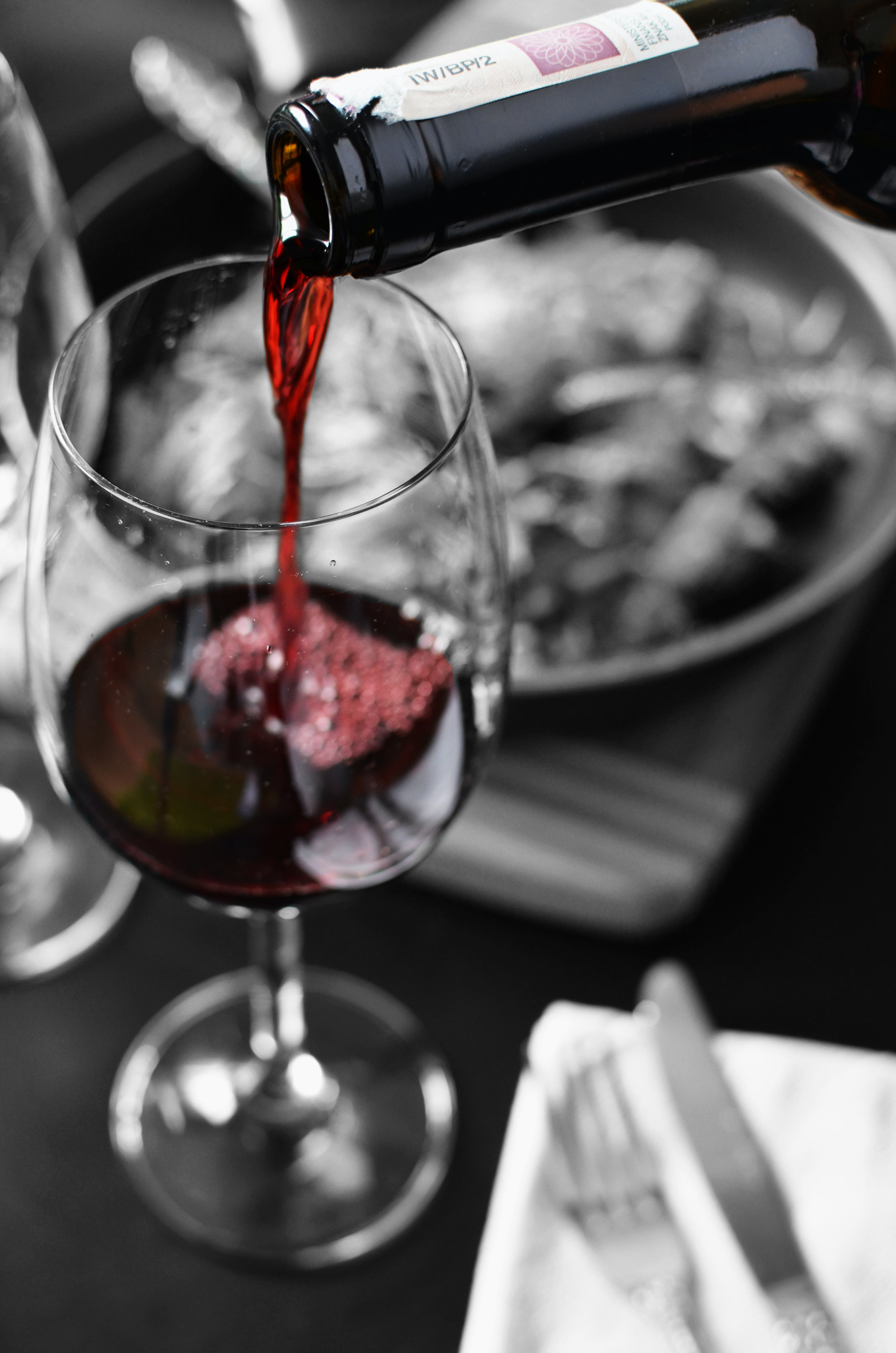 Schwarzweiß-Bild von einem Weinglas, in das roter Wein eingeschenkt wird.