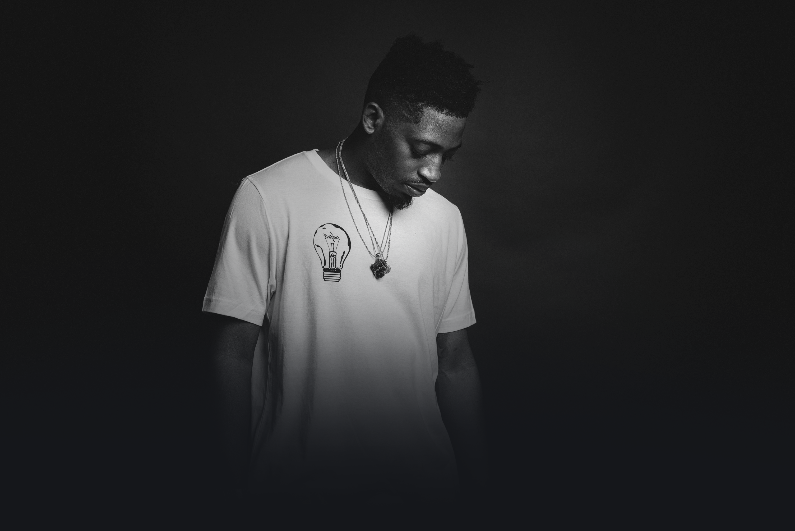 Person vor einem dunklen Hintergrund mit einem weißen T-Shirt, guckt auf den Boden.