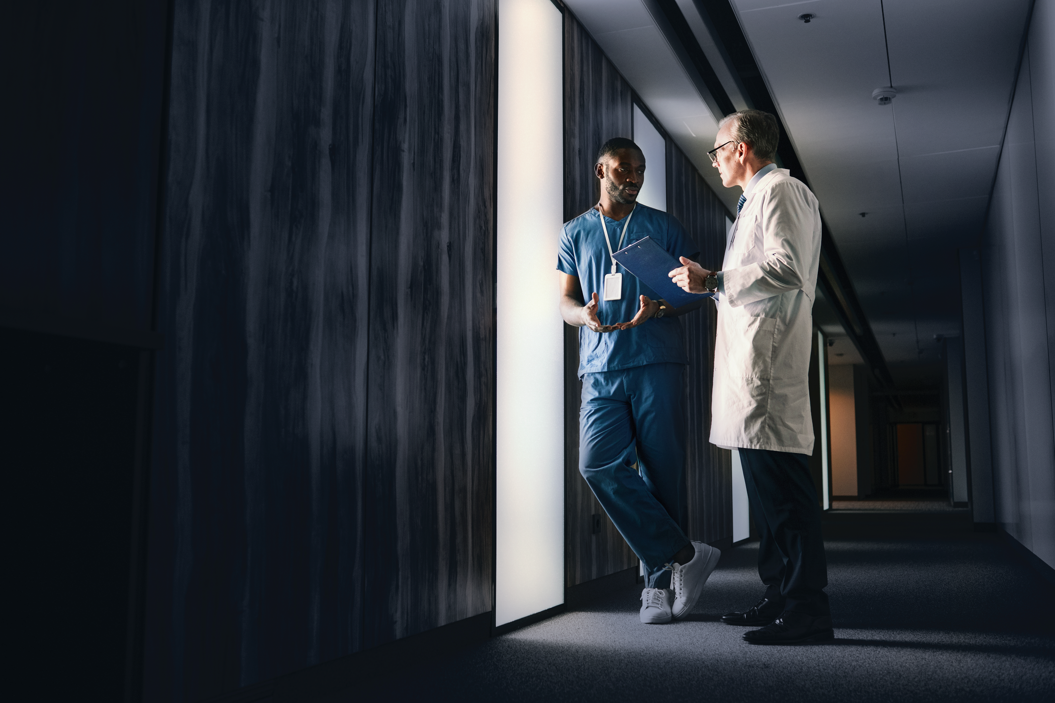 Zwei medizinische Fachkräfte stehen in einem Gang und unterhalten sich.