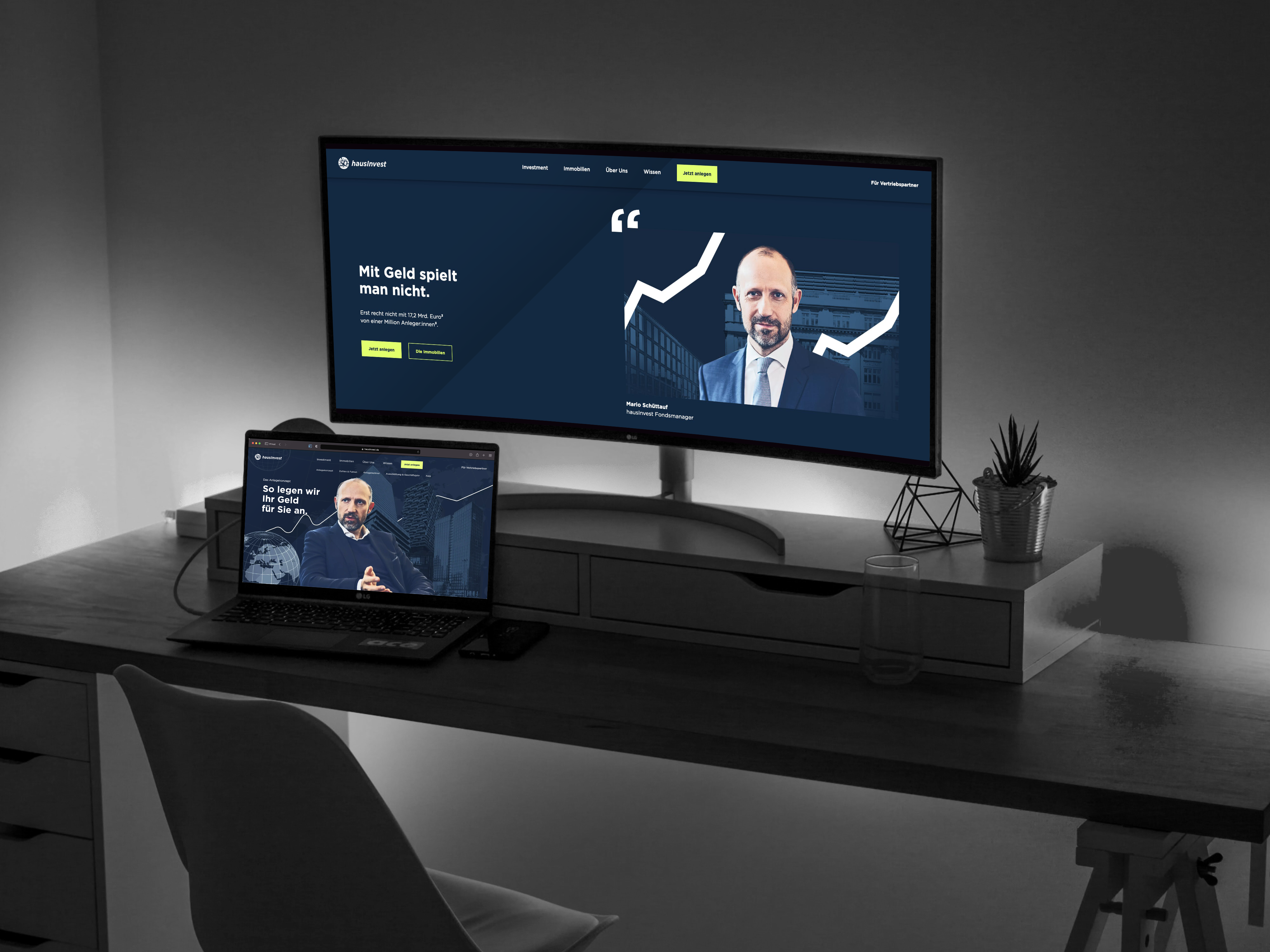Schreibtisch mit Laptop und Monitor, auf dem Elemente der hausInvest Website zu sehen sind.