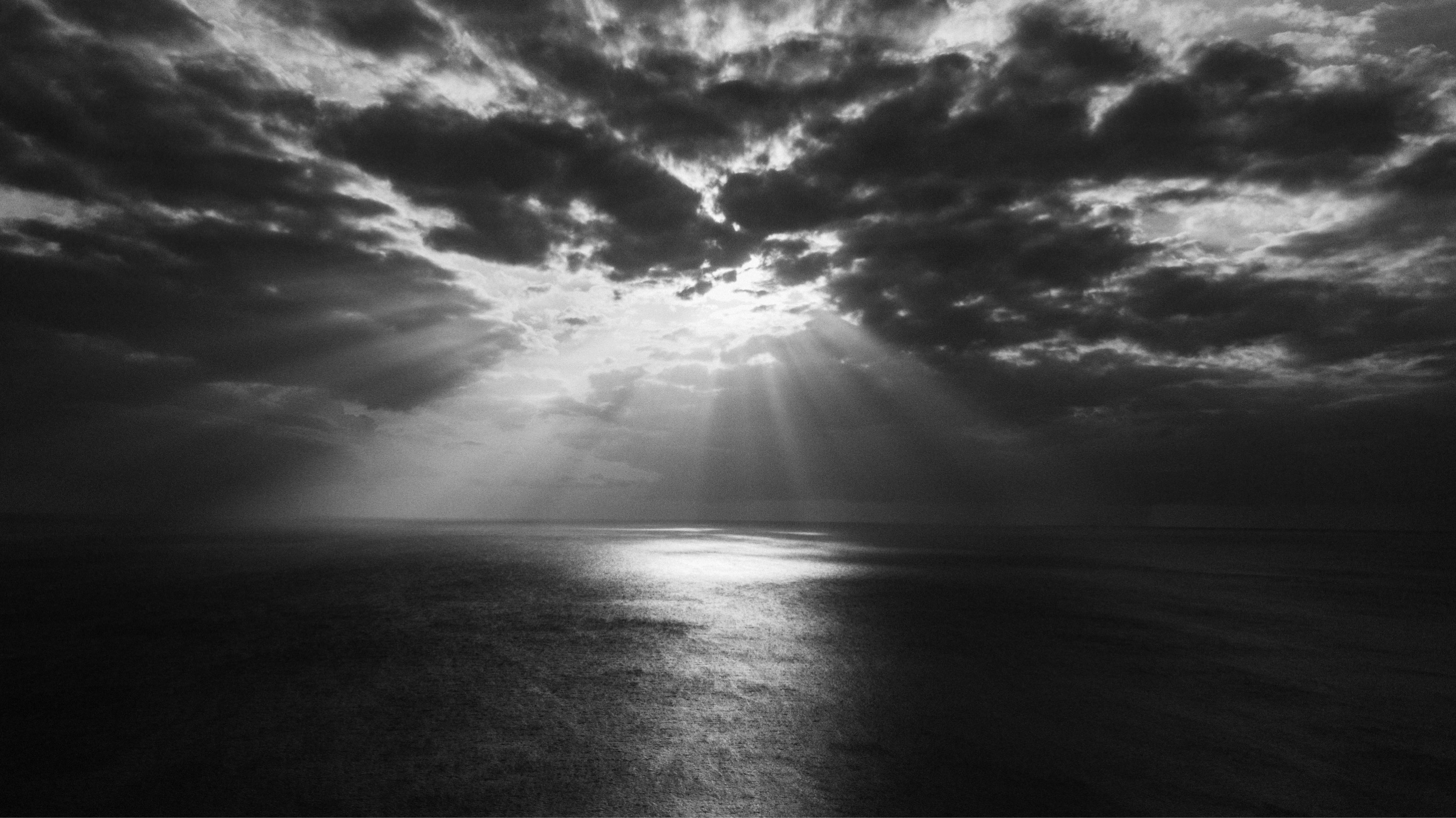 Meer unter einer Wolkendecke, durch die einige helle Sonnenstrahlen dringen.
