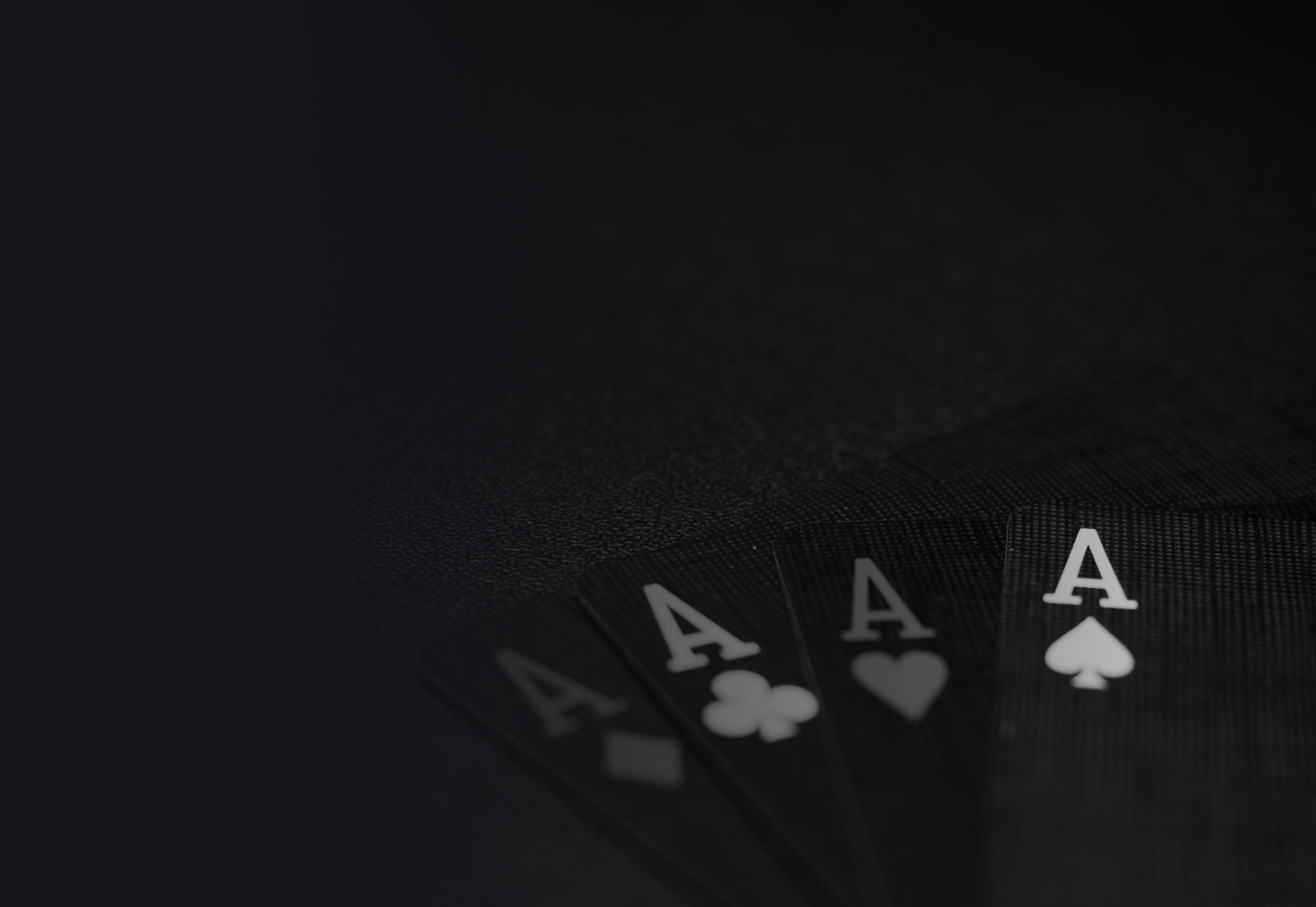 Ein schwarzer Hintergrund, auf dem in einer Ecke vier Spielkarten mit weißen Ass-Symbolen zu sehen sind.