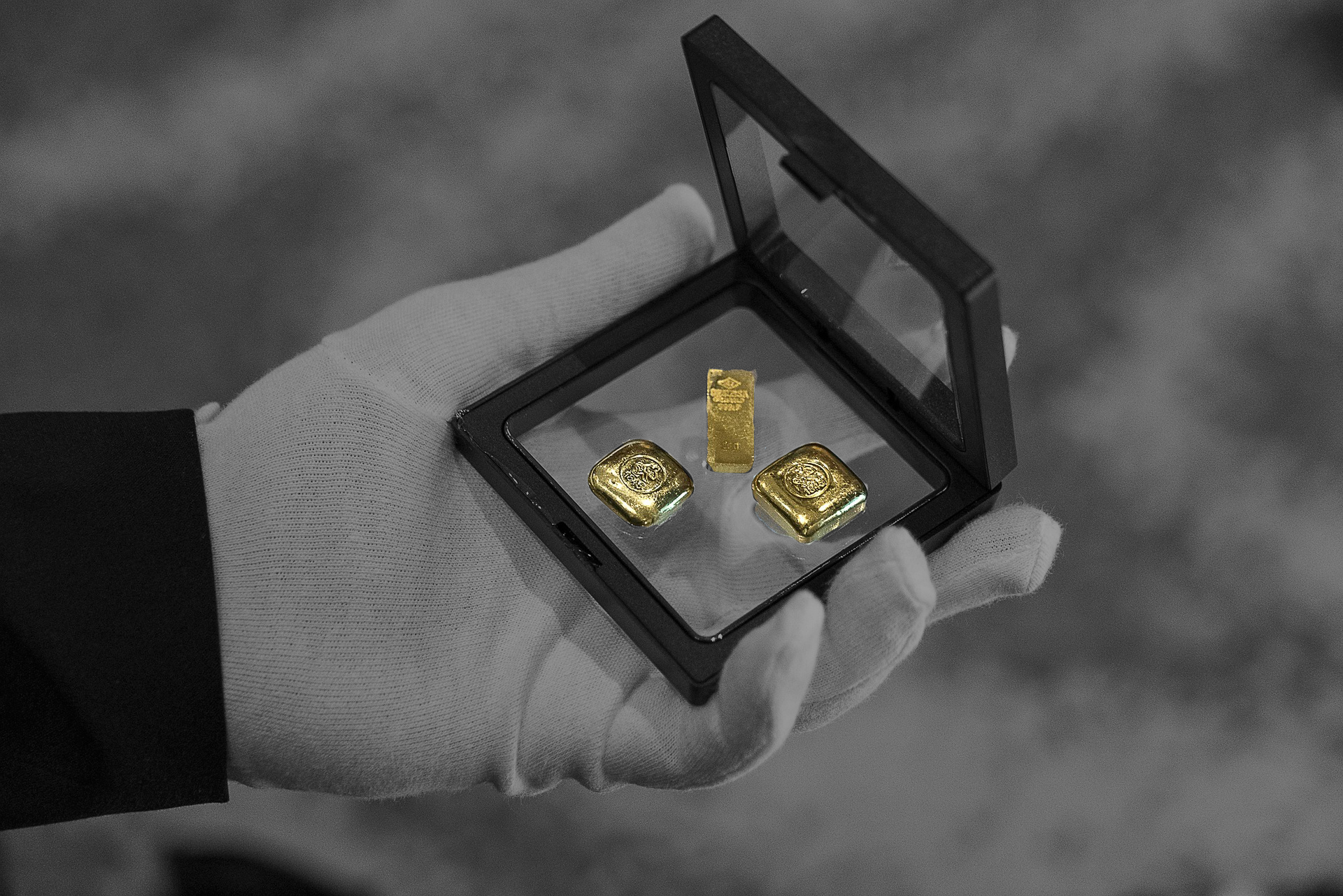 Eine Hand hält eine Glasschatulle mit mehreren kleinen Goldbarren.