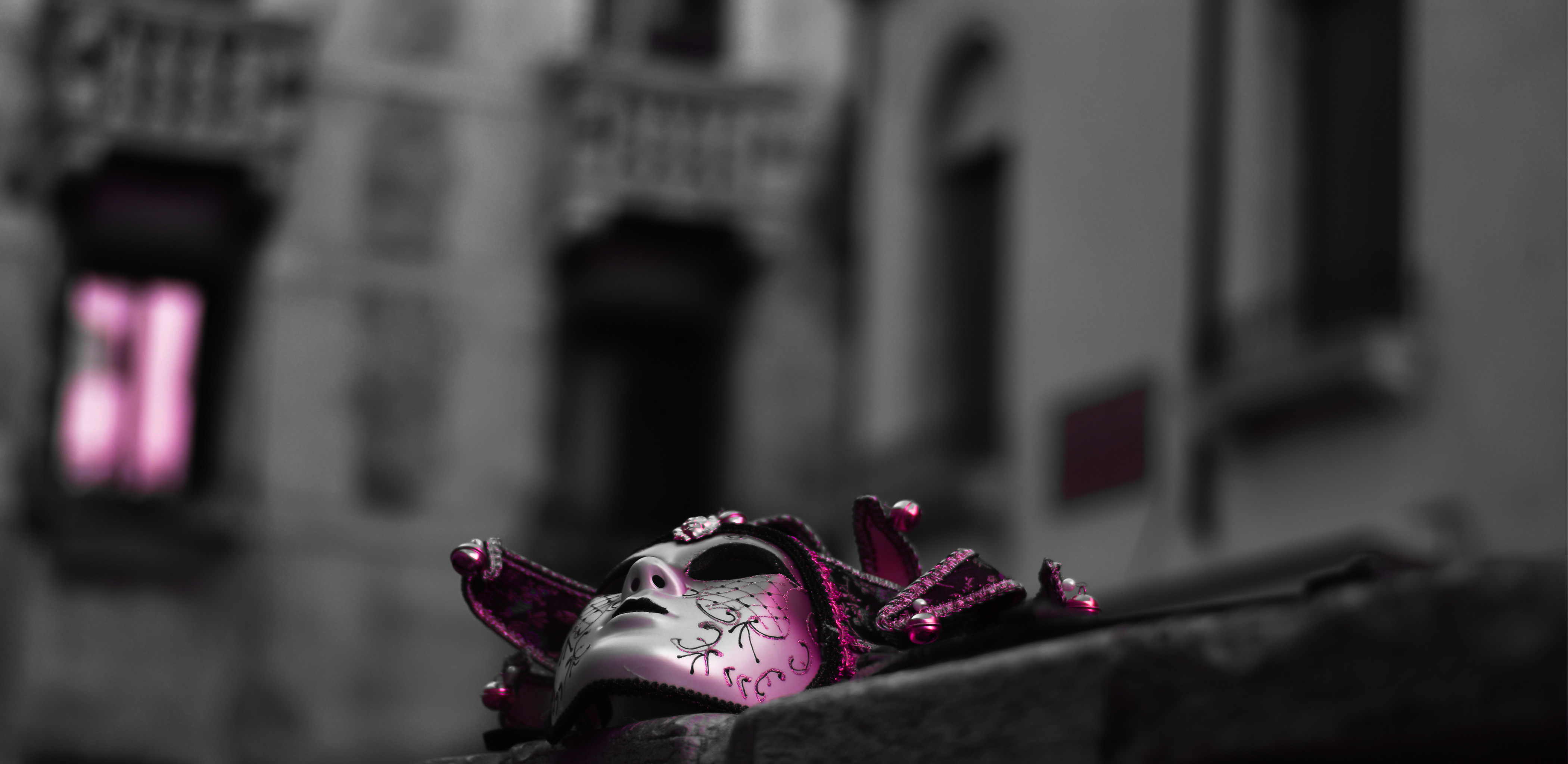 Verzierte Theatermaske liegt auf einer Mauer, im Hintergrund ein altes Gebäude mit Balkonen.