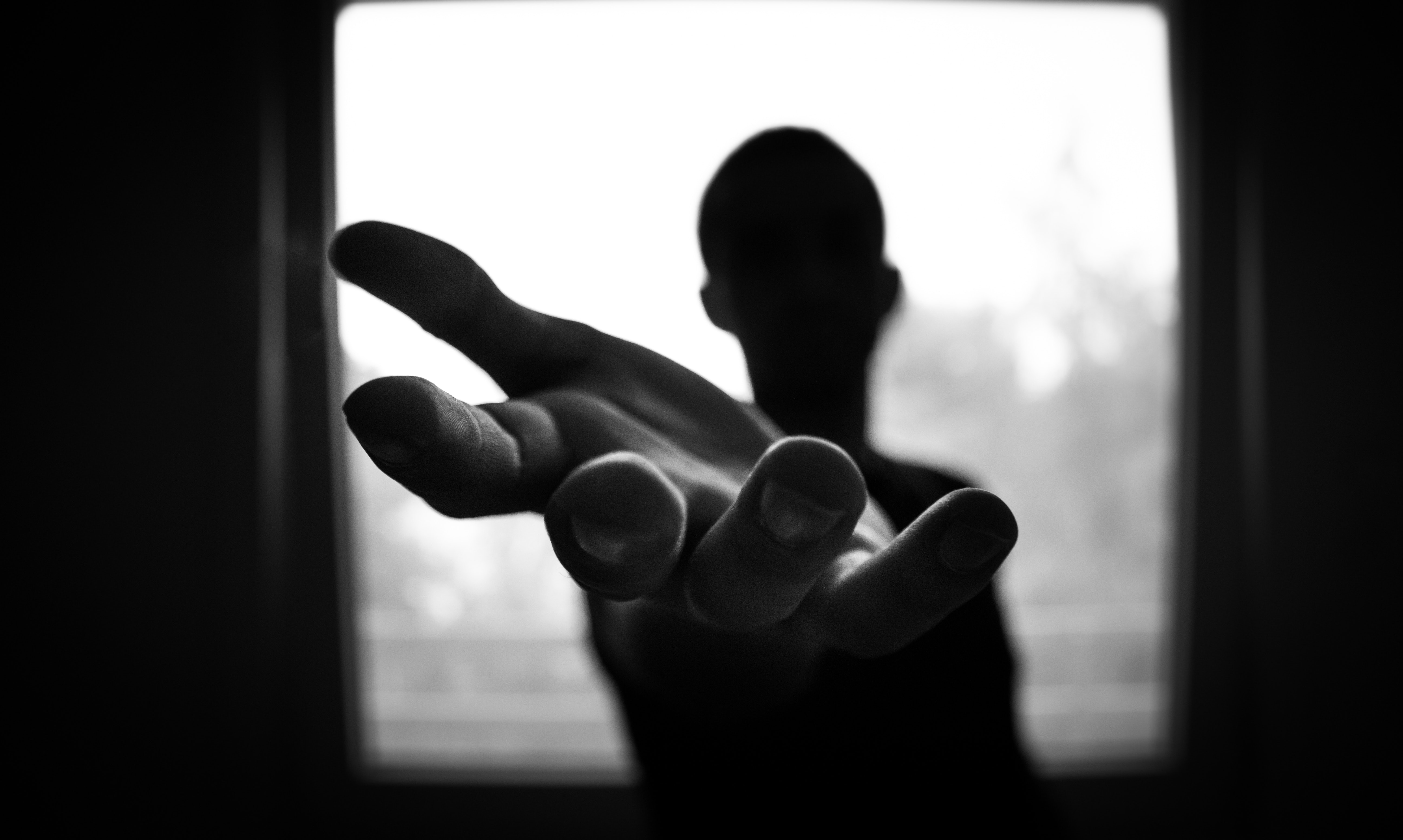 Silhouette von Person vor hellem Fenster, die Hand geradeaus ausgestreckt.